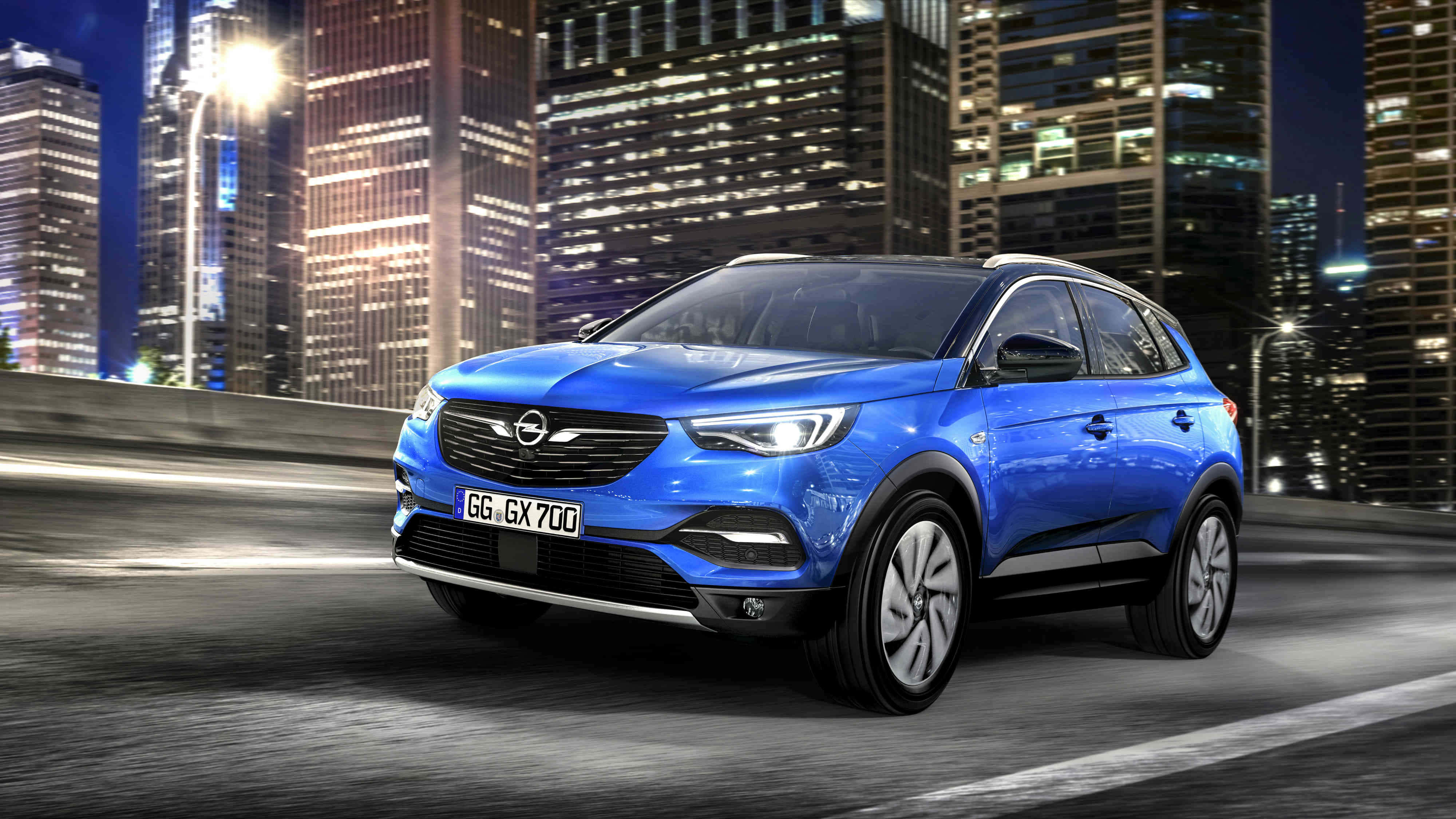 Opel Grandland X 桌布 壁紙 — 一輛鮮藍色的歐寶SUV在夜間的城市高速公路上飛馳，背後是發光的摩天大樓。