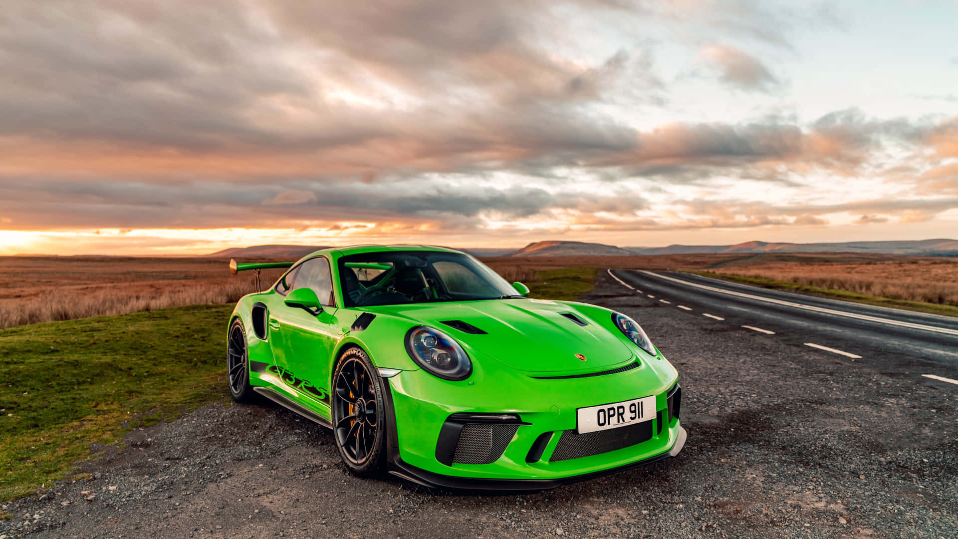  壁紙 — 一輛鮮綠色保時捷911 GT2 RS停放在日落時分蜿蜒道路旁的碎石路肩上，天空有戲劇性的雲彩。
