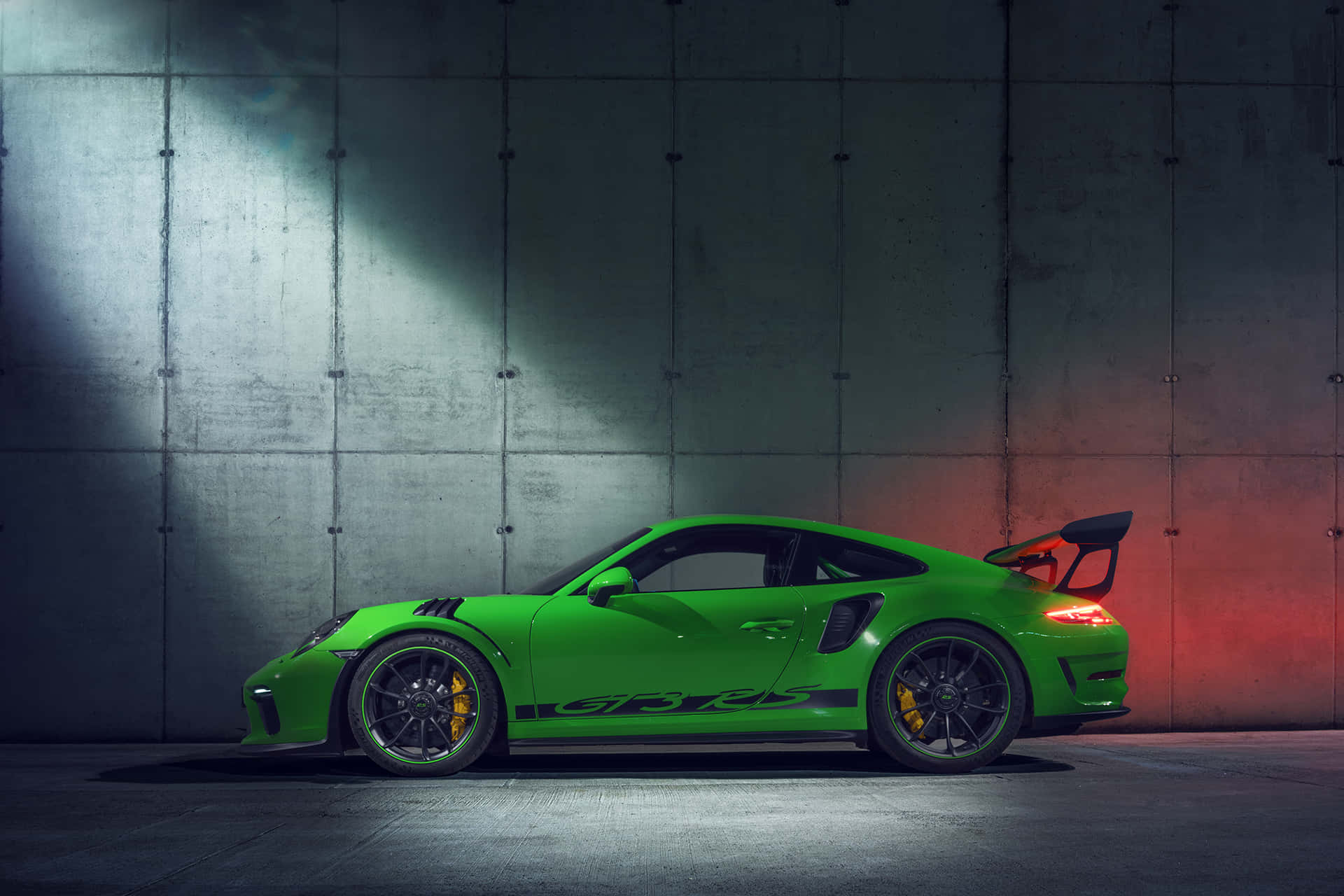  壁紙 — 一輛鮮綠色保時捷911 GT3 RS跑車，在紋理混凝土牆前被對比鮮明的聚光燈戲劇性地照亮。