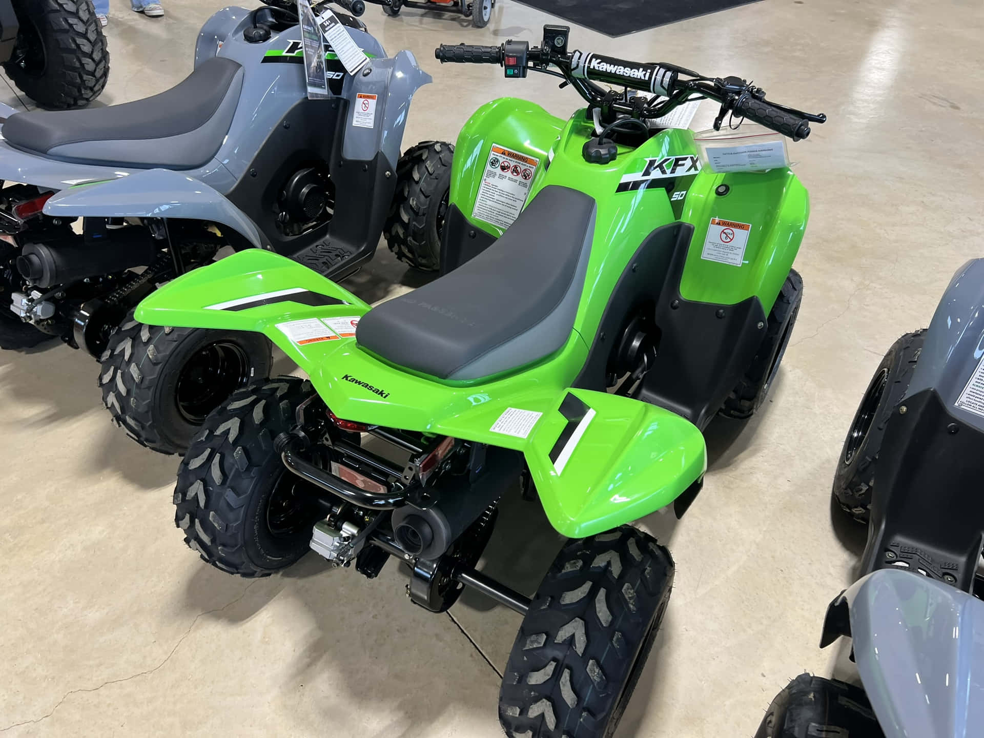  壁紙 — 鮮綠色的Kawasaki KFX 80 ATV在展示間展出，附近有其他ATV。