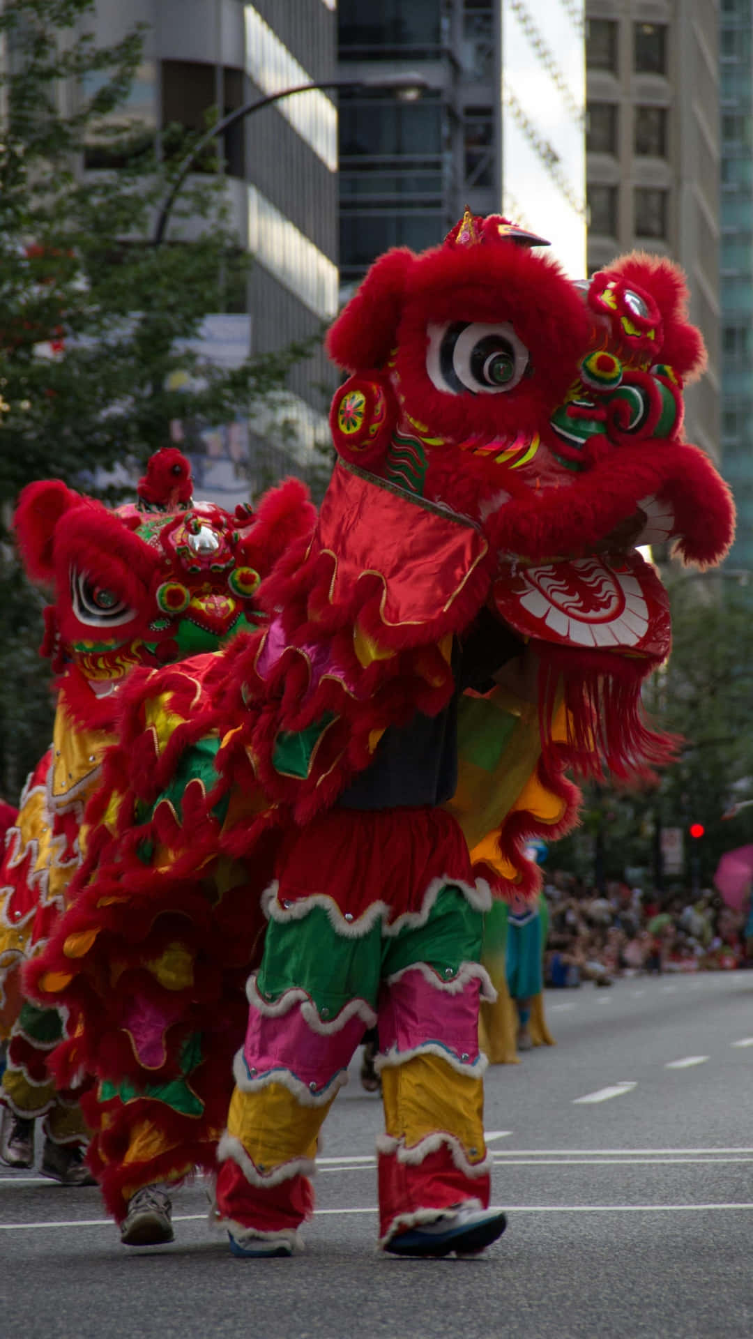 壁紙 — 鮮豔的紅色和金色舞獅服裝在節日遊行中於城市街道上充滿活力地表演。