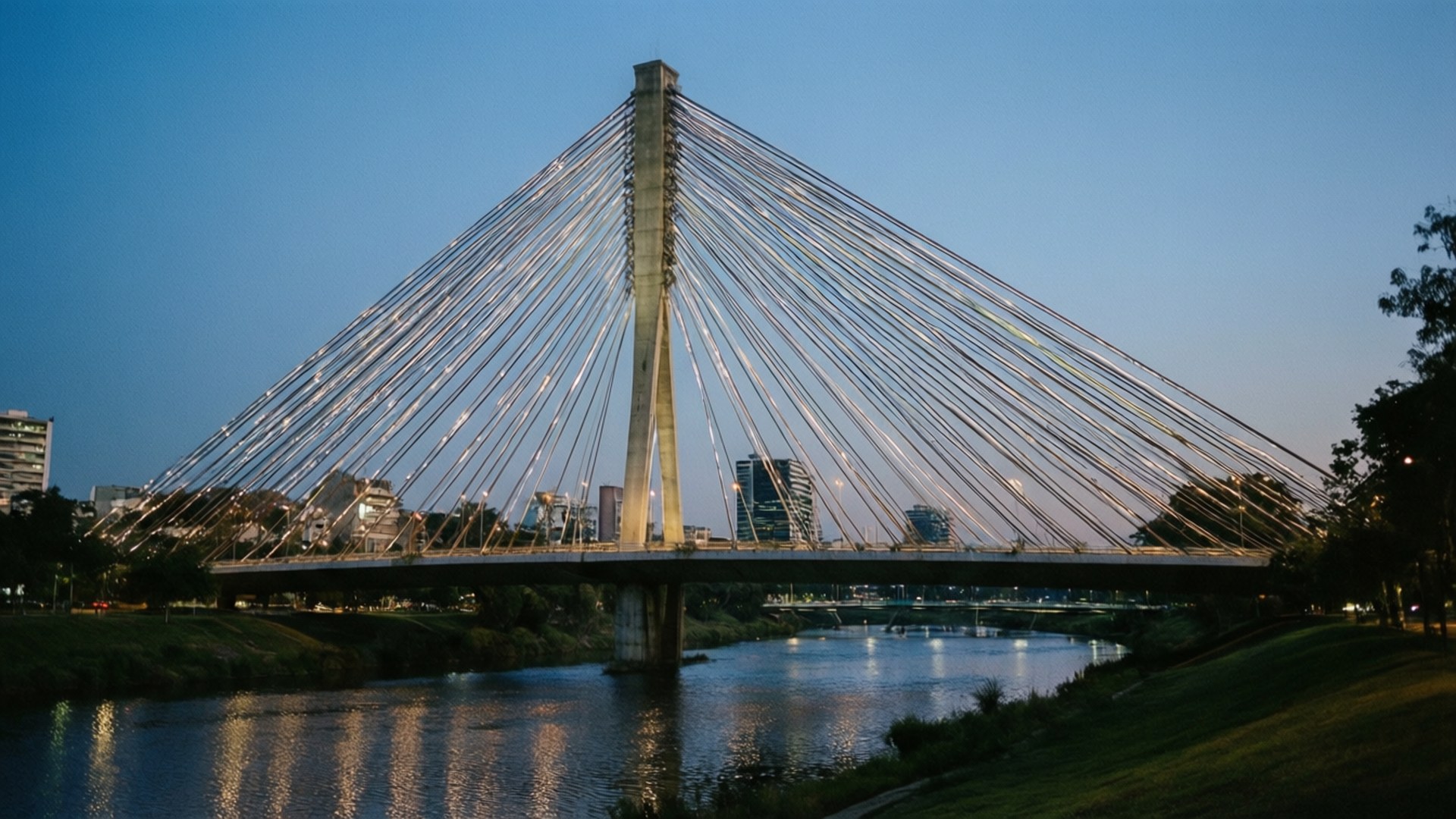 Puente de la Unidad Twilight 壁紙 — 一座現代斜張橋在暮色天空下散發溫暖燈光，其倒影在平靜的河面上閃爍。
