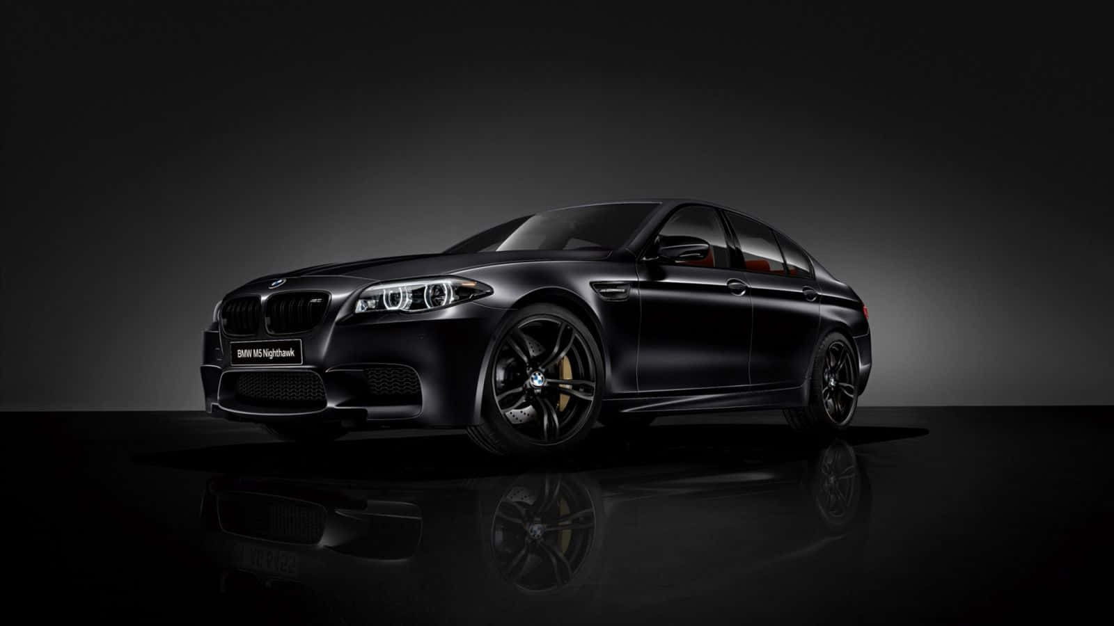Bmw M5 桌布 壁紙 — 一輛時尚的消光黑色BMW M5 Nightshade轎車在攝影棚燈光下閃耀，金色煞車卡鉗在深色漸層背景上清晰可見。