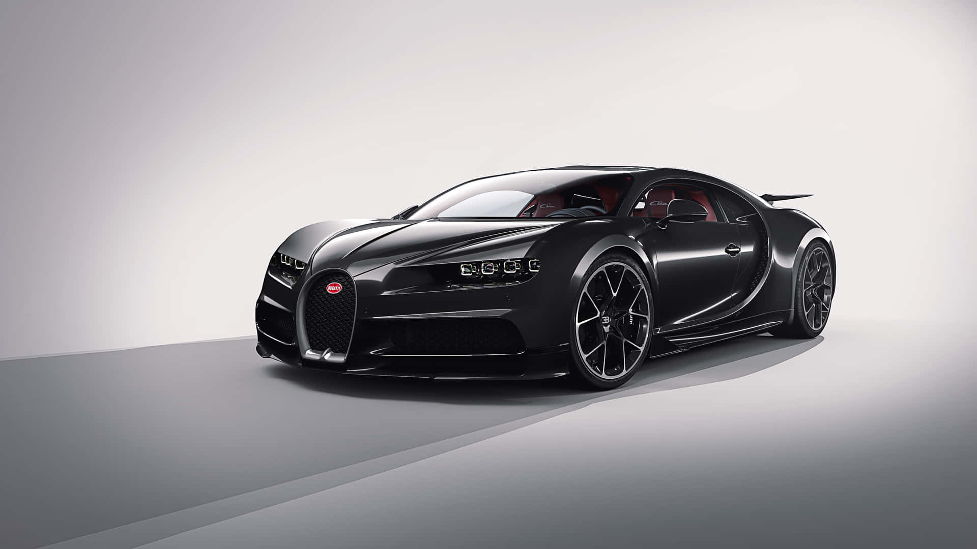 Bugatti Chiron 桌布 壁紙 — 一輛時尚的消光黑色Bugatti Chiron超級跑車，配備紅色內裝，在柔和燈光下停在簡約的灰色工作室地板上。