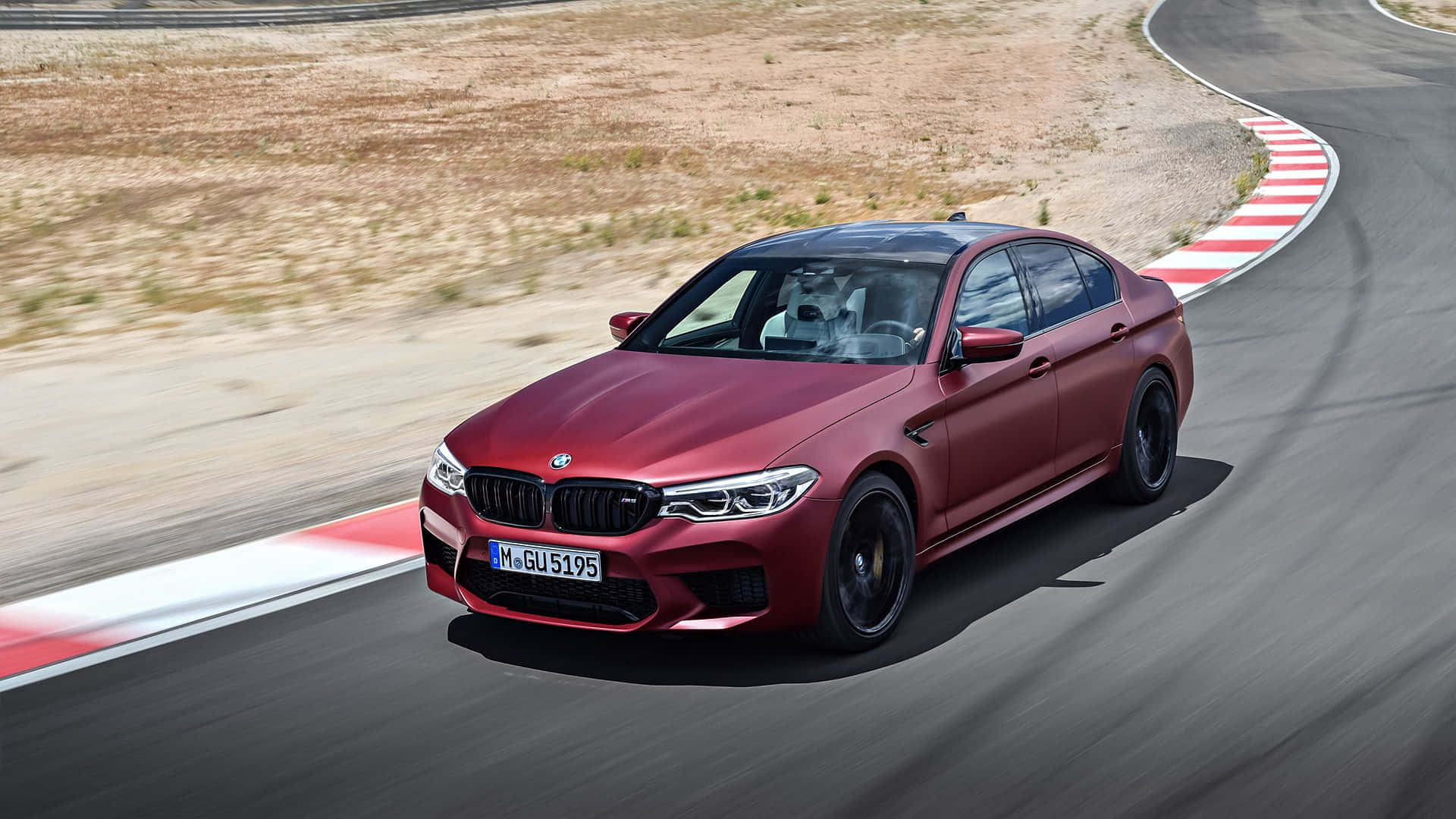 Bmw M5 桌布 壁紙 — 一輛消光紅色BMW M5房車在賽道上以模糊動態和紅白路緣石激進過彎。