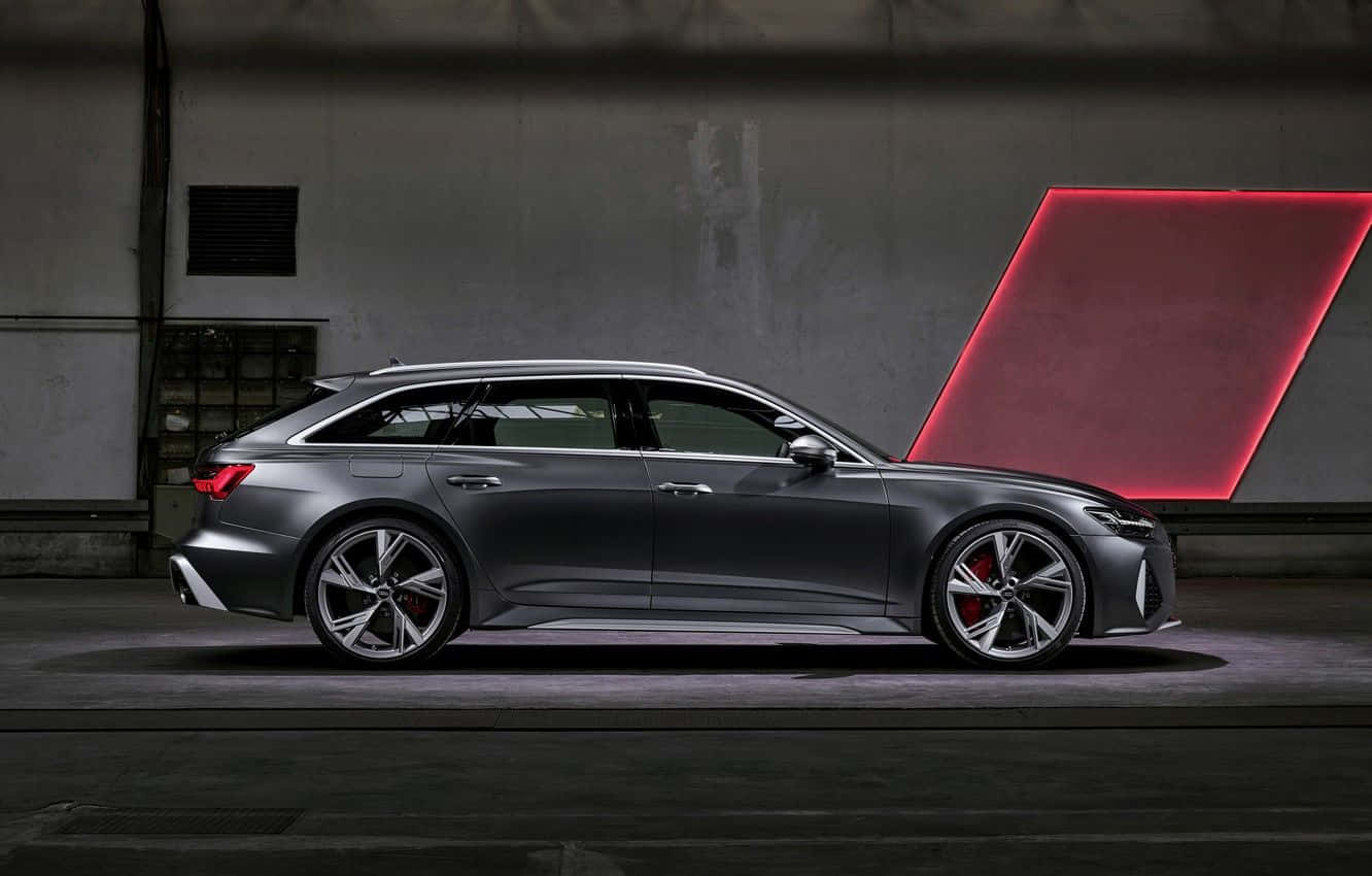 Audi Rs6 桌布 壁紙 — 一輛時尚的消光灰色奧迪RS6 Avant旅行車在昏暗的工業車庫中展示，背後有一個發光的紅色幾何燈板。