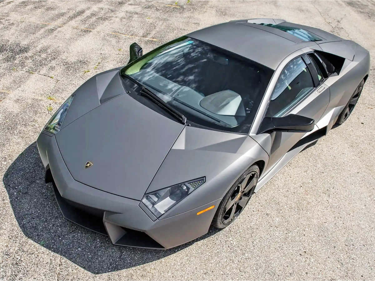 Lamborghini Reventón 桌布 壁紙 — 一輛消光灰色的藍寶堅尼跑車停在破裂的柏油路面上，在明亮的日光下。
