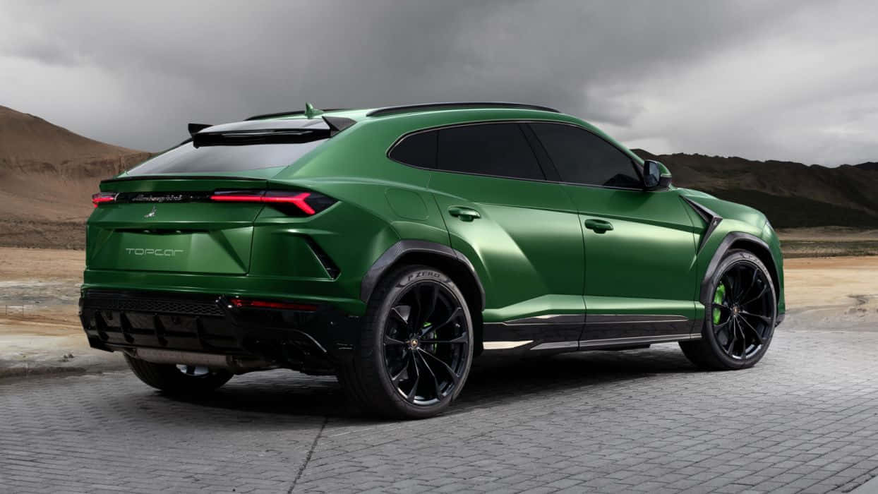 Lamborghini Urus 桌布 壁紙 — 一輛消光綠色的藍寶堅尼 Urus 停放在鋪砌路面上，天空多雲，背景是乾燥的山丘。