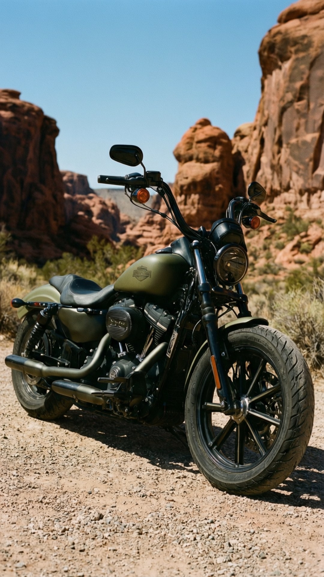 Desert Canyon Custom 壁紙 — 一輛啞光橄欖綠色的哈雷戴維森摩托車停泊在礫石上，背景是紅色岩石地貌，天空清澈湛藍。