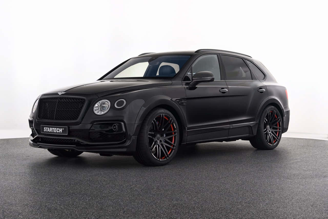 Bentley Bentayga 桌布 壁紙 — 一輛啞光黑色的賓利 Bentayga，配備紅色制動卡鉗和 Startech 調校，在白色背景下的灰色工作室地板上蓄勢待發。