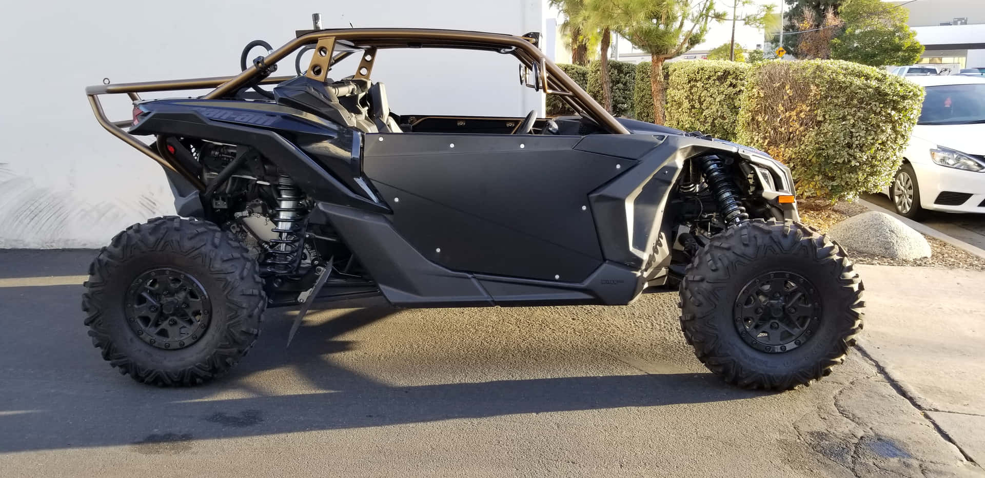  壁紙 — 一輛啞光黑色的全地形車，配備大型凸塊輪胎，在明亮的日光下停在瀝青路面上。