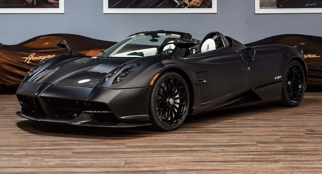 Pagani Zonda C12 Roadster 桌布 壁紙 — 一輛線條流暢的啞光黑色帕加尼Huayra敞篷跑車，搭配白色內裝，停放在豪華展示間的木地板上。