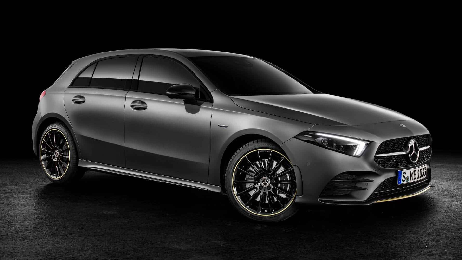 Mercedes Benz A-class 桌布 壁紙 — 一輛時尚的啞光灰色賓士A-Class掀背車，配備黑色輪圈和金色飾邊，在深色工作室背景中展示。