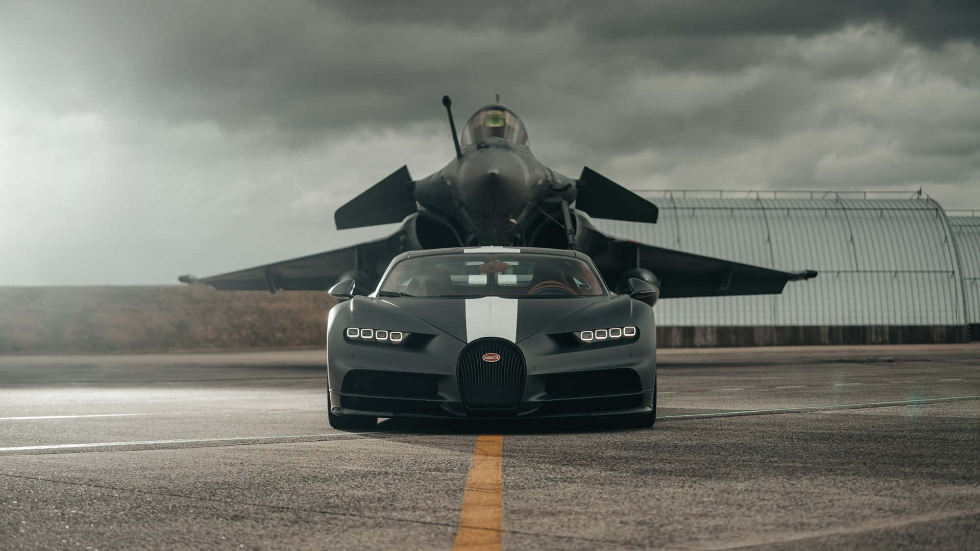Bugatti Chiron 桌布 壁紙 — 一輛啞光灰色的布加迪Chiron停在跑道上，身後有一架戰鬥機在暴風雨的天空下若隱若現。