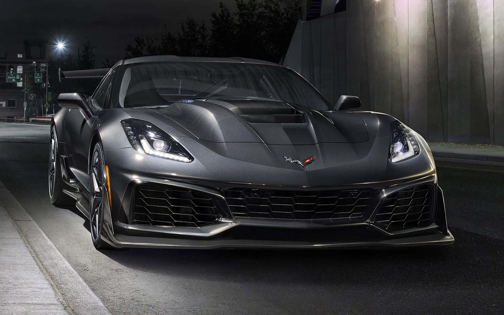 corvette 桌布 壁紙 — 一輛啞光灰色的Corvette跑車在夜間停放在潮濕的城市街道上，在街燈下閃閃發光。