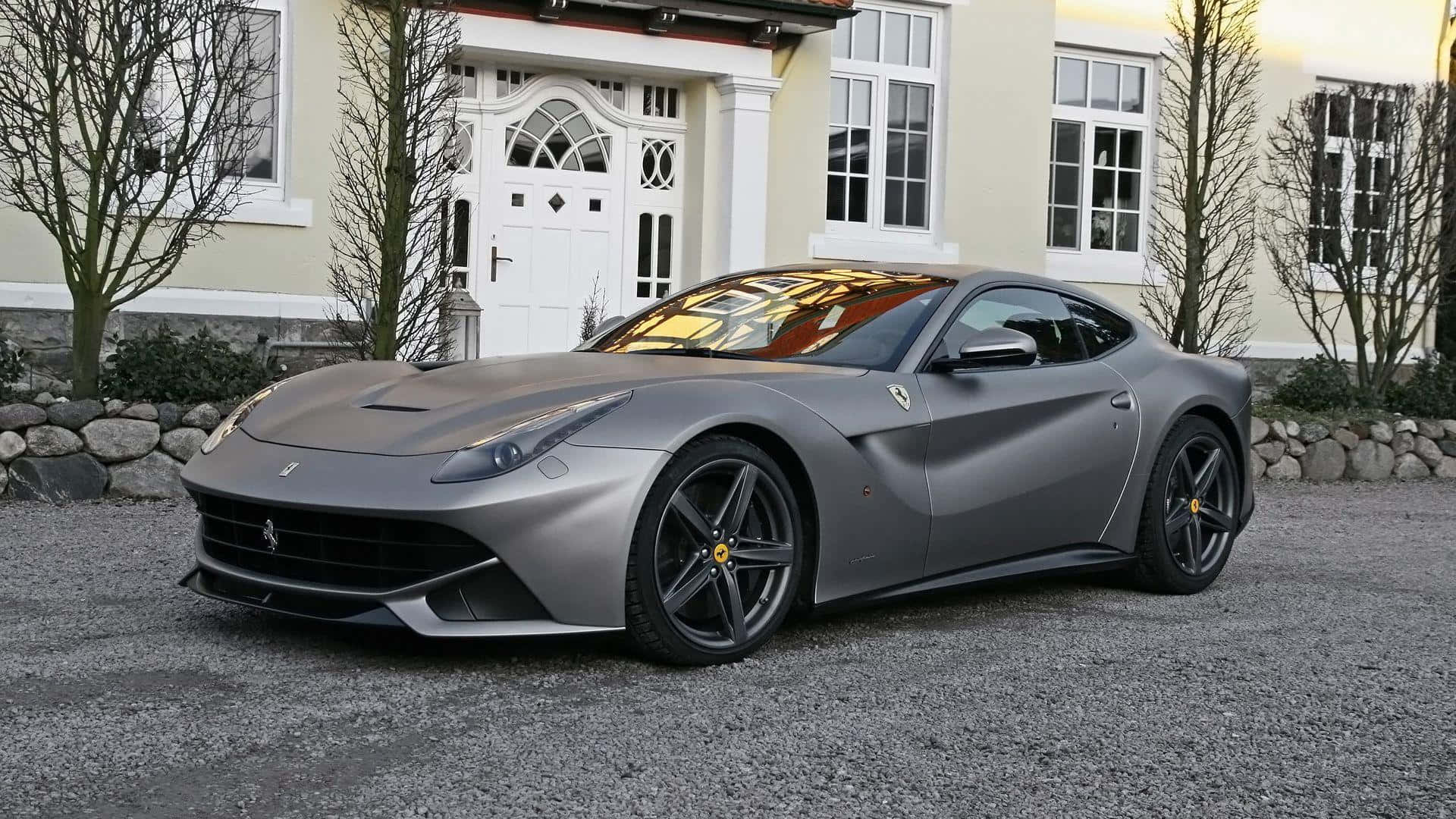 Ferrari F12 Berlinetta 桌布 壁紙 — 一輛啞光灰色的法拉利F12停泊在碎石路上，前面是一間有禿樹的大奶油色房子。