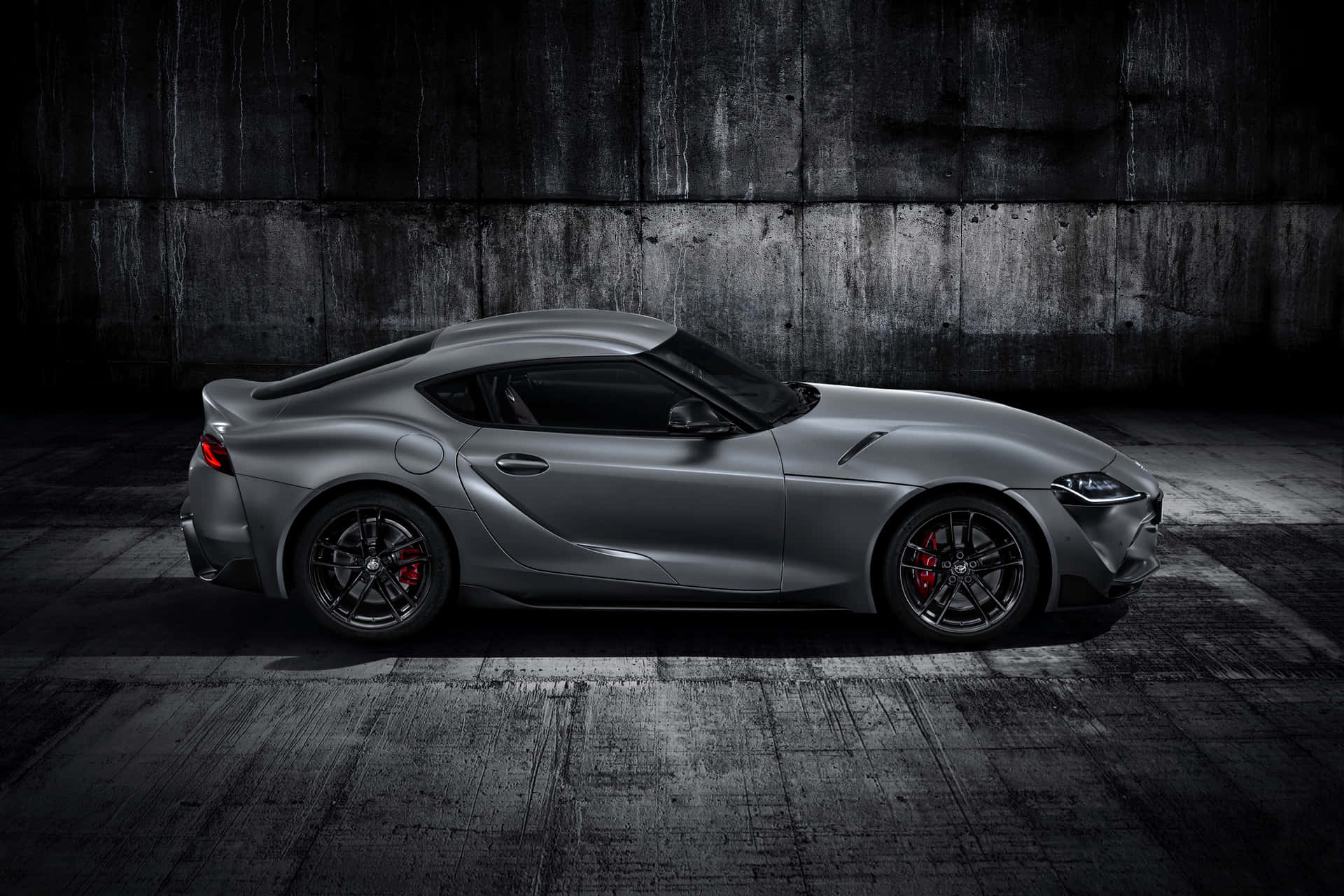 啞光灰色跑車配紅色制動器，以深色混凝土牆為背景。 — Toyota Supra 壁紙