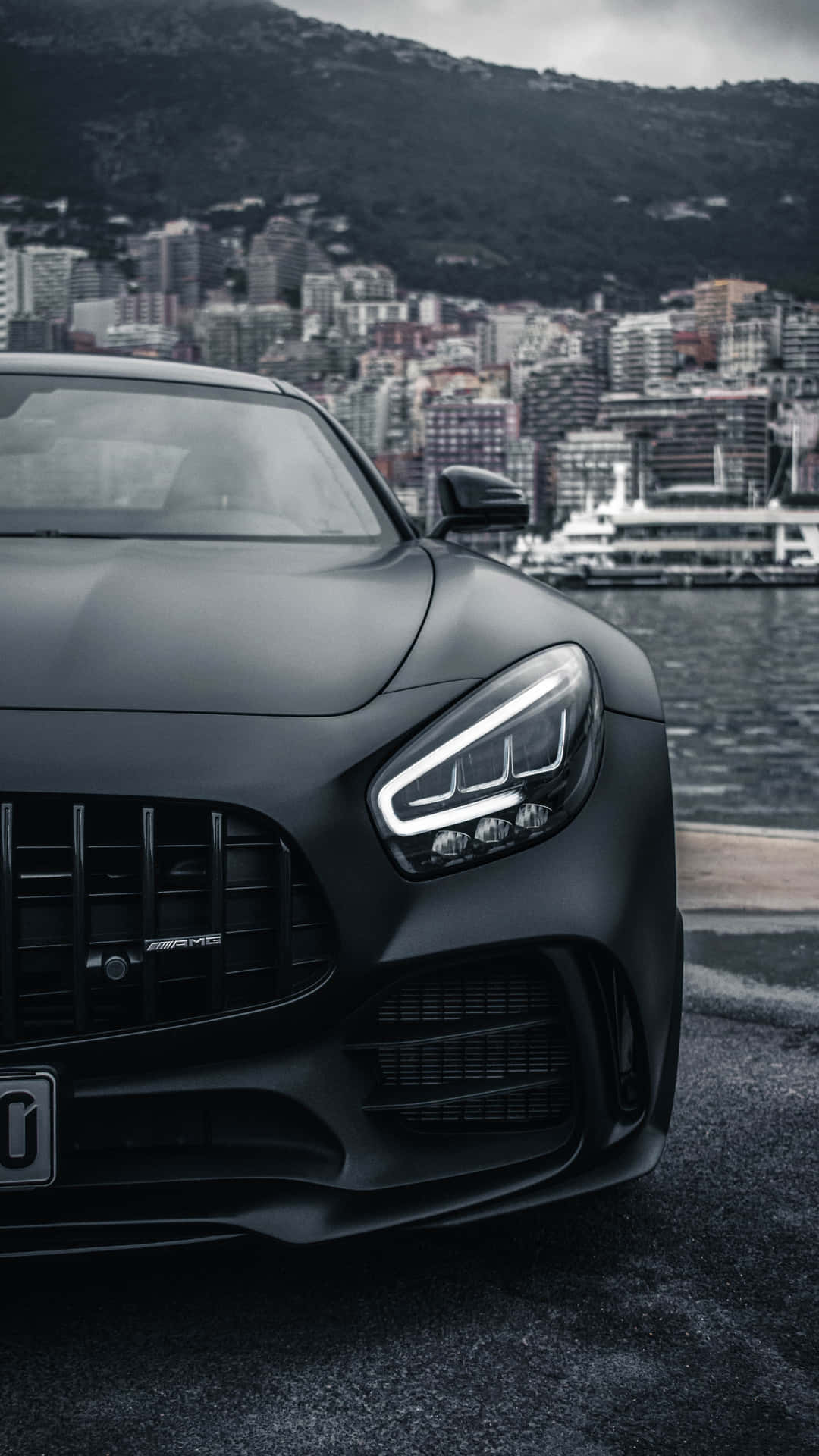 啞黑色AMG跑車停泊在海濱，背後有城市和山脈。 — Amg Gt R 壁紙