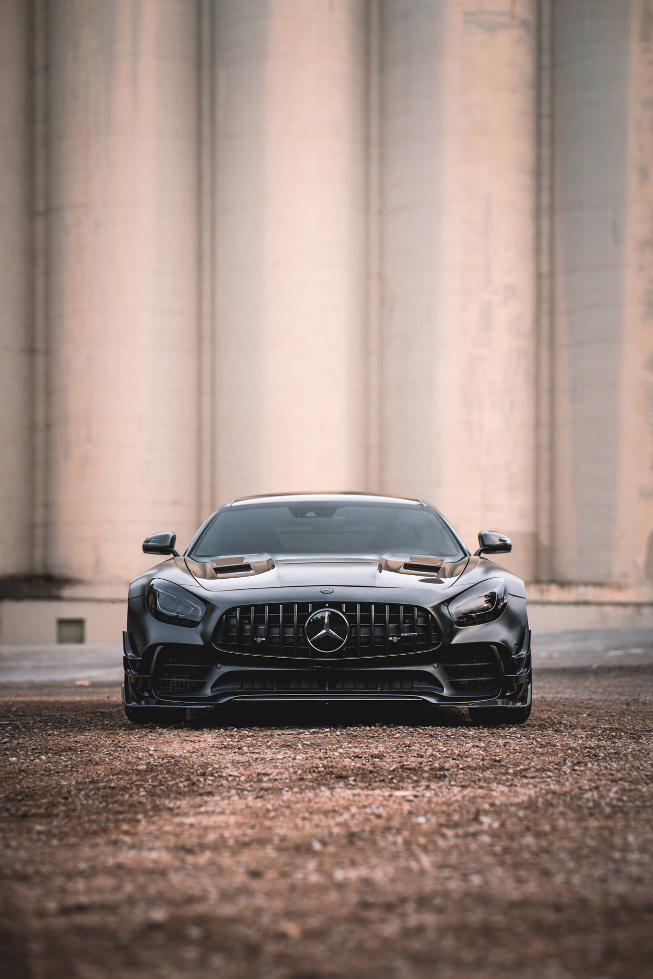 啞黑色 Mercedes-AMG GT R 停放在混凝土柱前的礫石上。 — Amg Gt R 壁紙