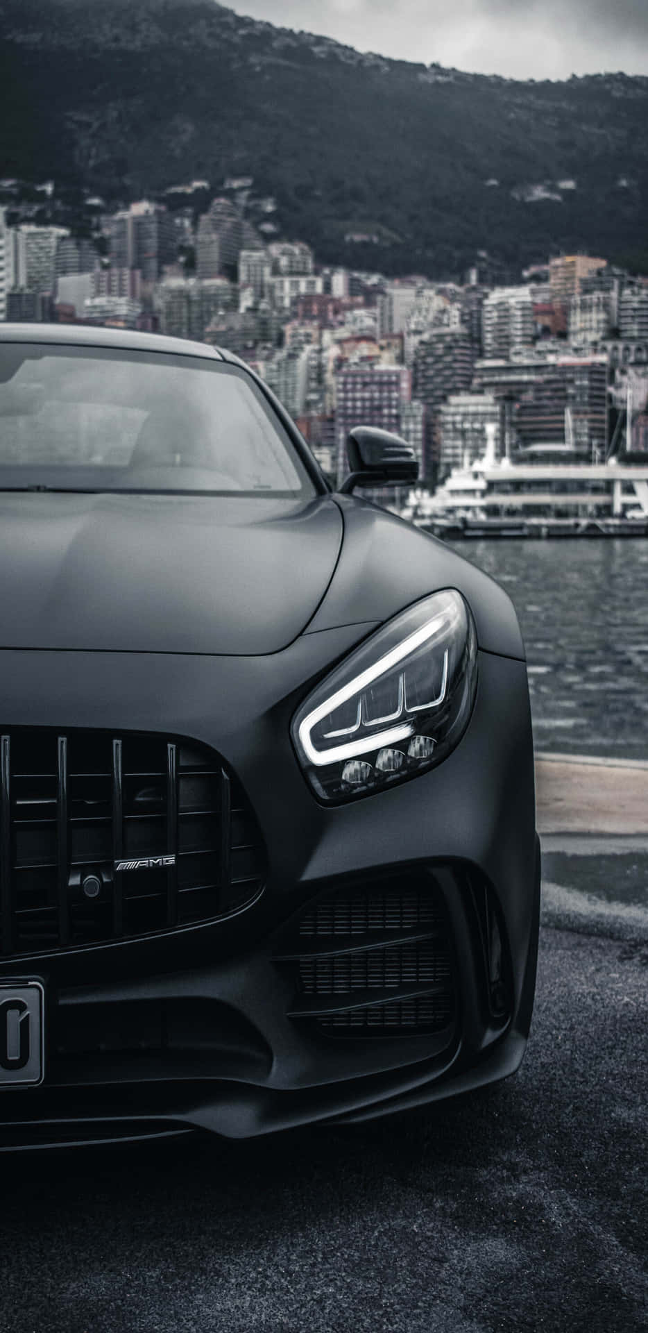 啞黑色AMG跑車停泊在水邊，後面有城市和山脈。 — Amg Gt R 壁紙