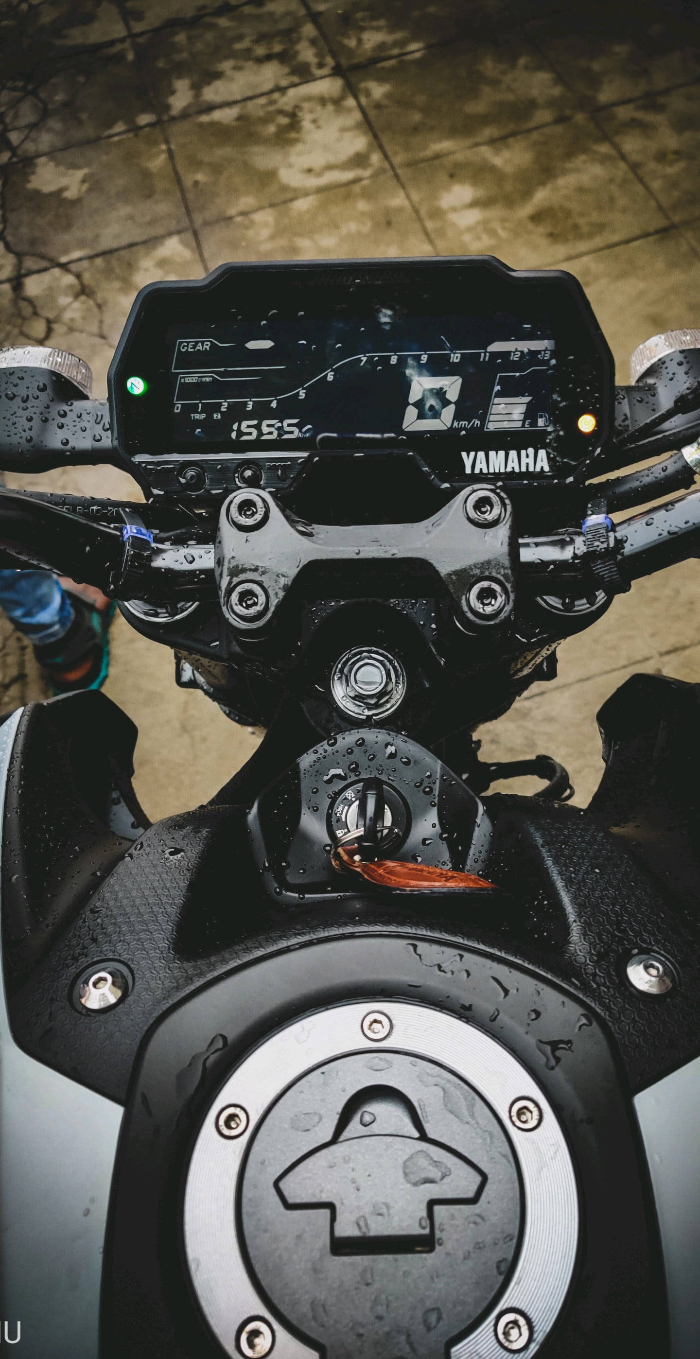 yamaha mt 15 桌布 壁紙 — Yamaha機車潮濕的儀表板和油箱特寫，雨滴在黑色和銀色表面上閃閃發光。