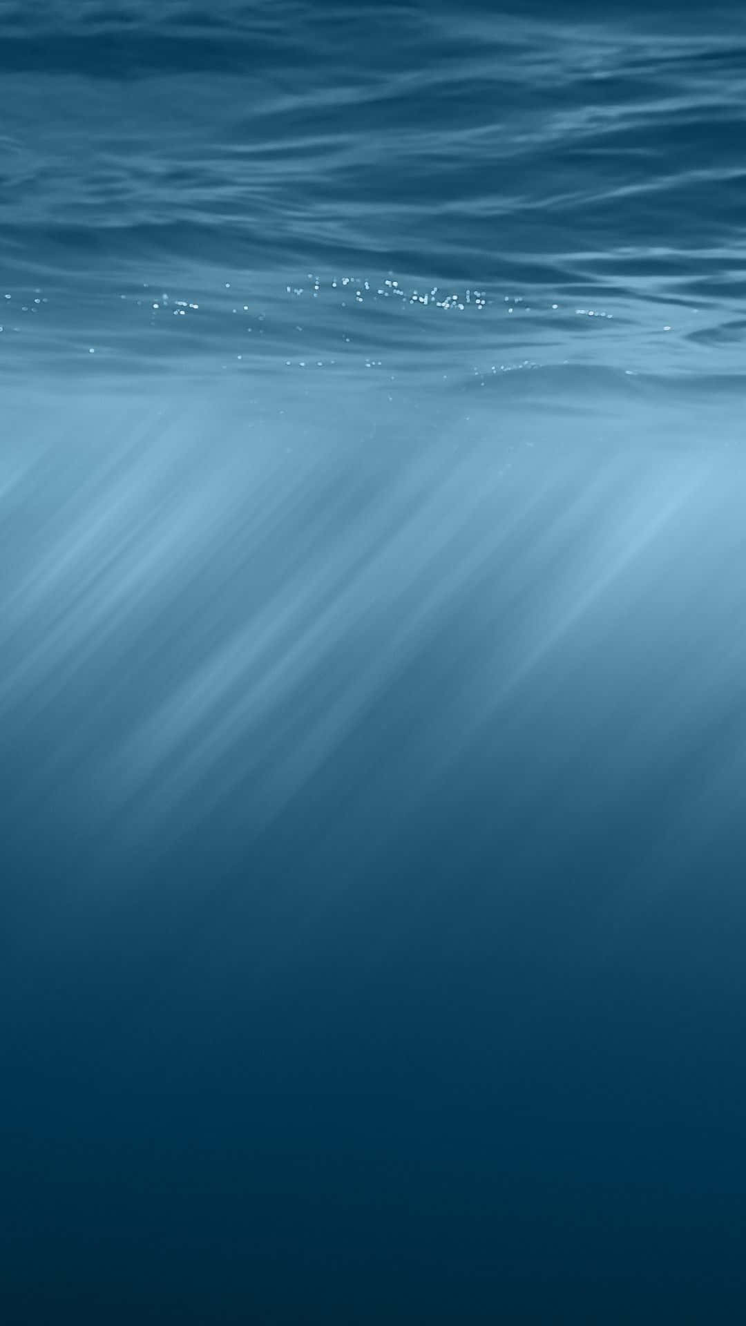  壁紙 — 陽光穿透平靜的海浪，在水下投射出空靈的藍色光線。