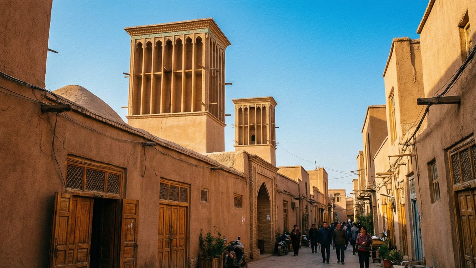 Yazd Windcatchers Alley 壁紙 — 陽光照耀的狹窄小巷，兩旁是陶土建築，傳統風塔在清澈的藍天下聳立。