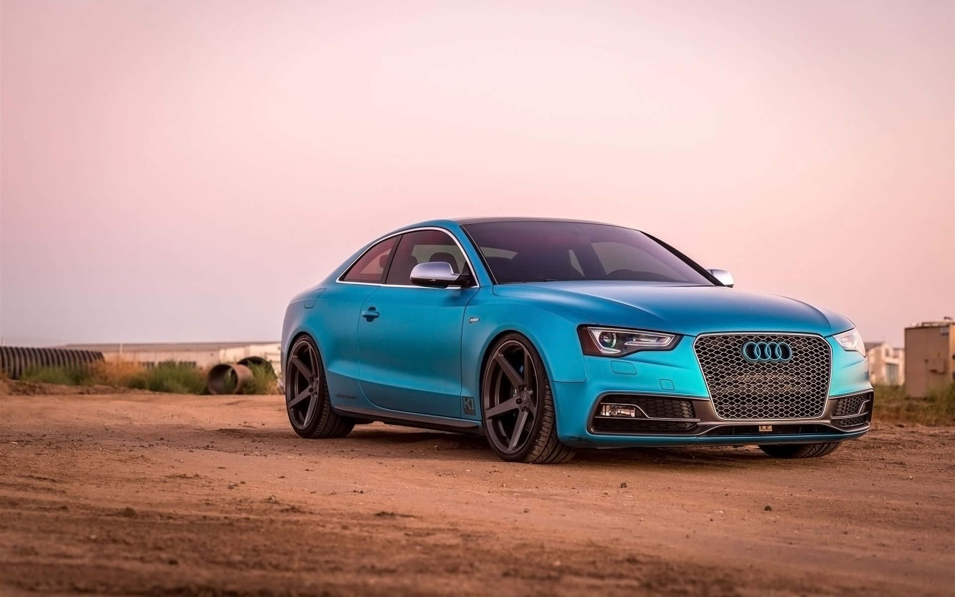 Audi S5 桌布 壁紙 — 一輛充滿活力的藍綠色奧迪轎跑車停在塵土飛揚的路邊，背景是柔和的粉紅色日落天空。