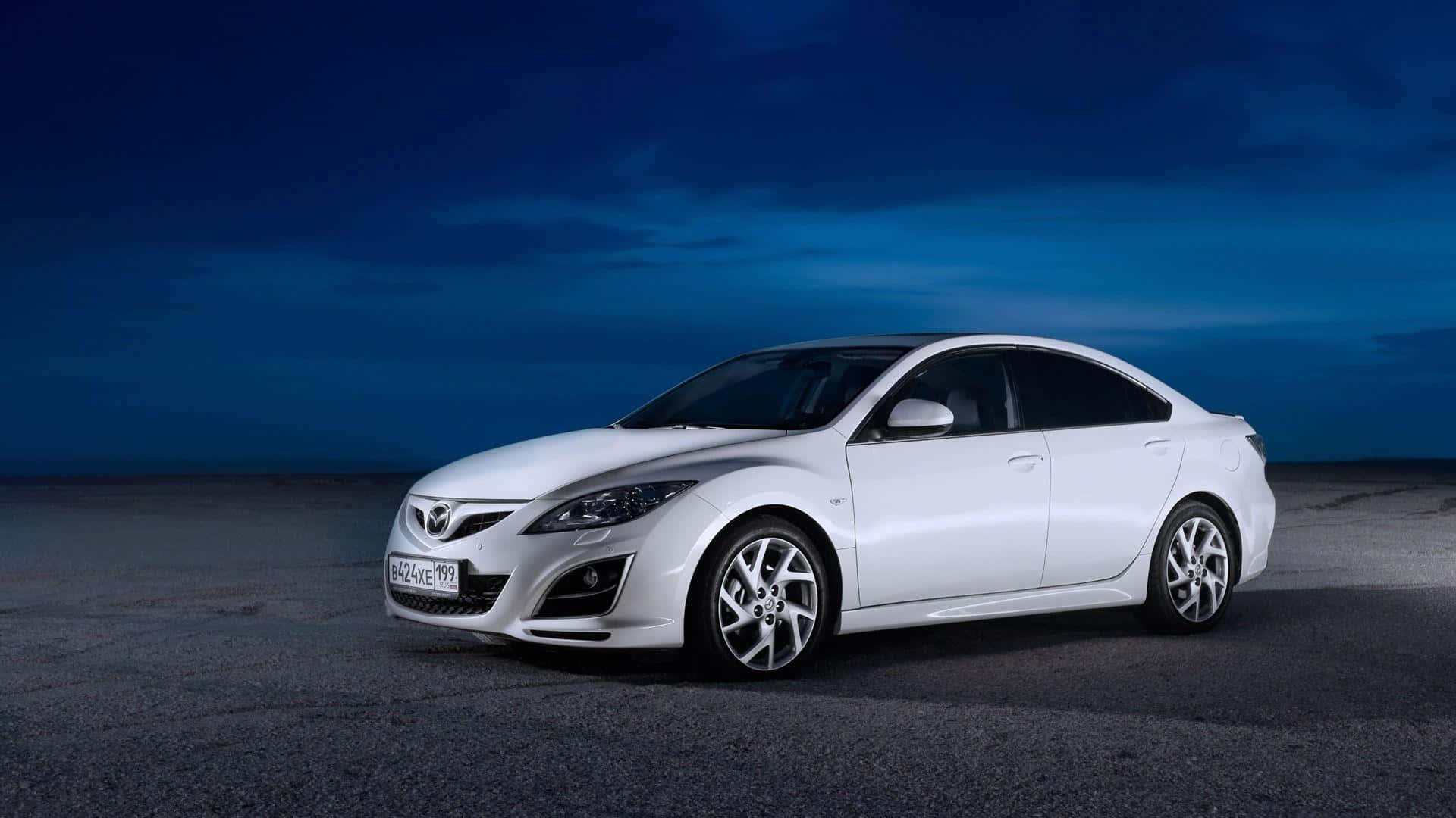 Mazda 6 桌布 壁紙 — 一輛時尚的白色馬自達轎車在暮色天空下，在廣闊的空曠瀝青路面上閃閃發光。