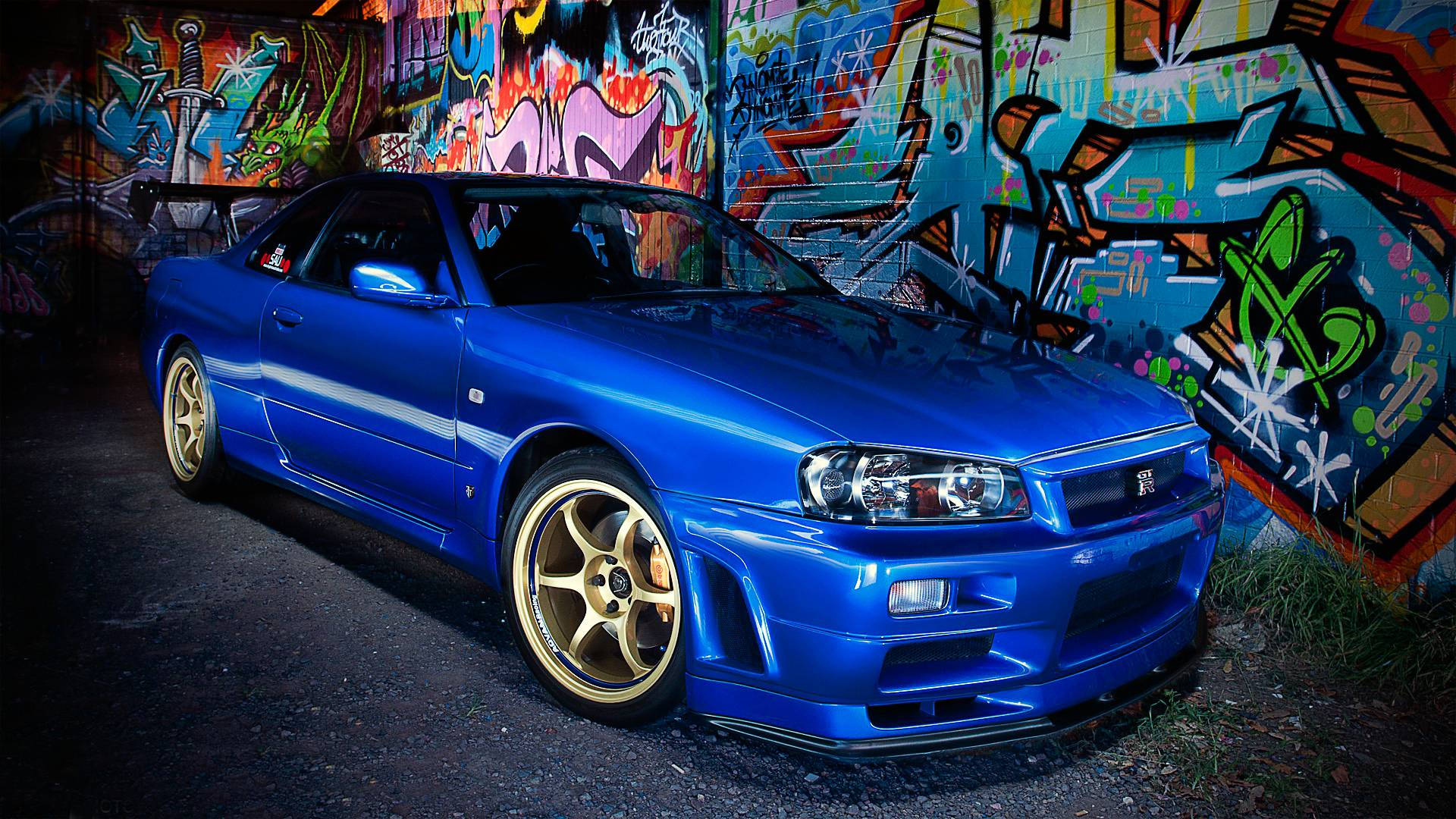 藍色跑車配金色輪圈夜晚停在塗鴉牆前。 — 日產 Skyline GTR R34 壁紙