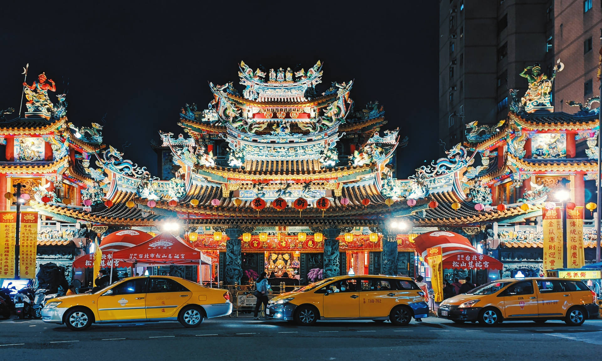 夜晚中明亮照明的傳統寺廟，外面停著黃色計程車。 — 台北 壁紙