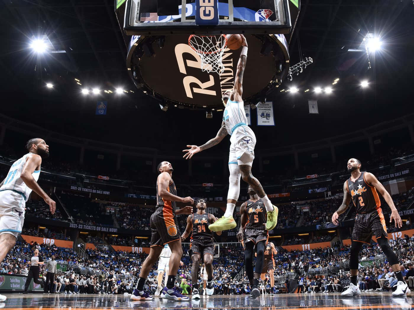 籃球運動員在擠滿觀眾的場館中，在空中越過防守球員灌籃。 — NBA 壁紙