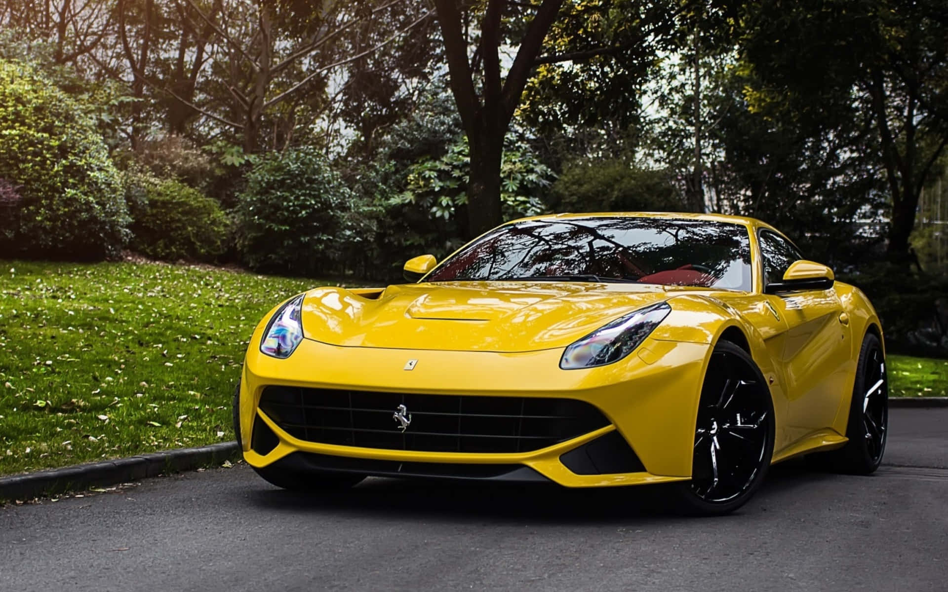 Ferrari F12 Berlinetta 桌布 壁紙 — 一輛充滿活力的黃色法拉利跑車在柔和日光下閃耀，停泊在樹木成行的瀝青路上。