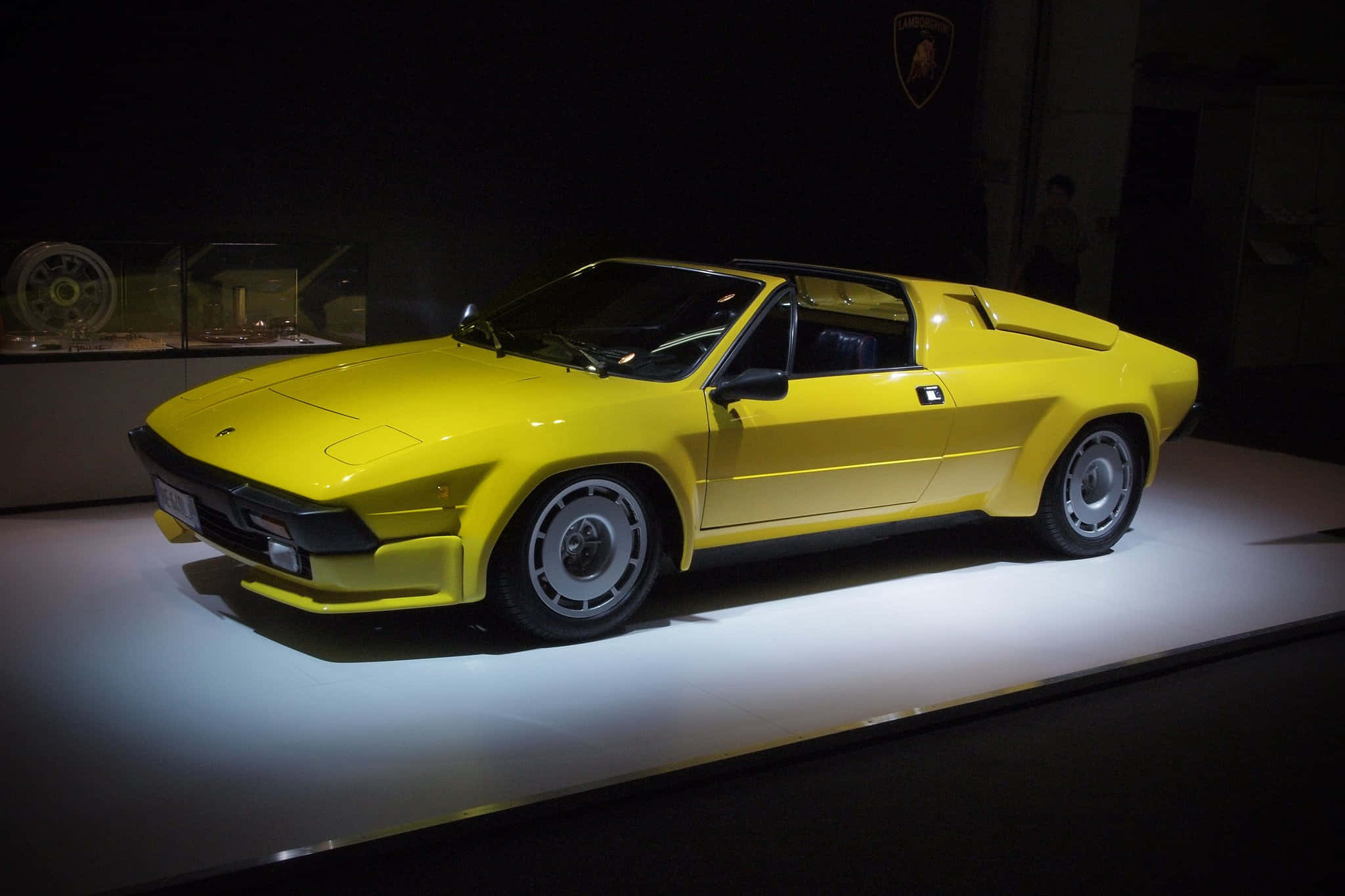Lamborghini Silhouette 桌布 壁紙 — 一輛鮮黃色的藍寶堅尼Countach跑車在黑暗的博物館環境中，於白色展示台上在聚光燈下閃閃發光。