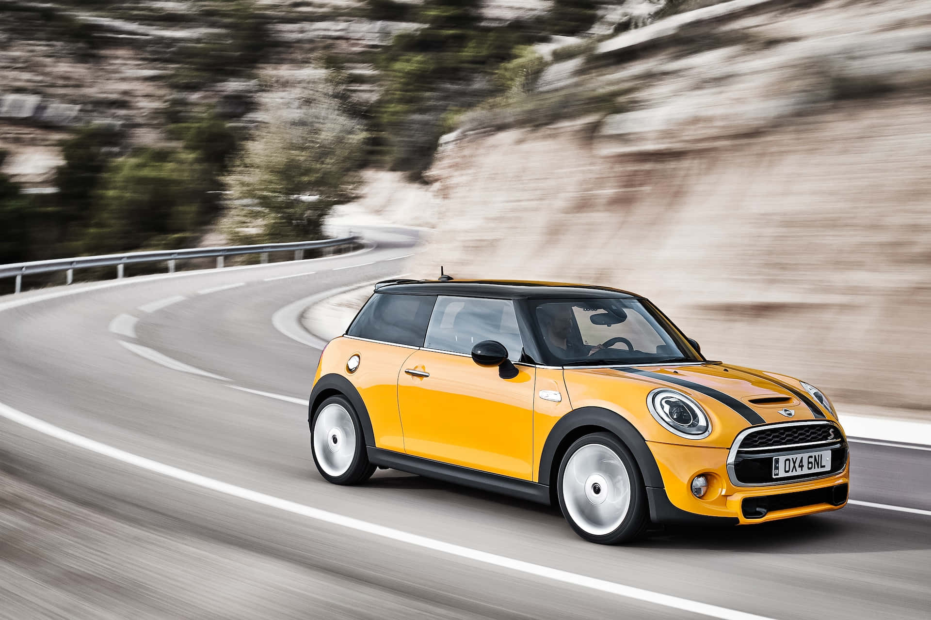 Mini Cooper S 桌布 壁紙 — 一輛鮮黃色的Mini Cooper沿著蜿蜒的山路疾馳，模糊的風景強調了動感。