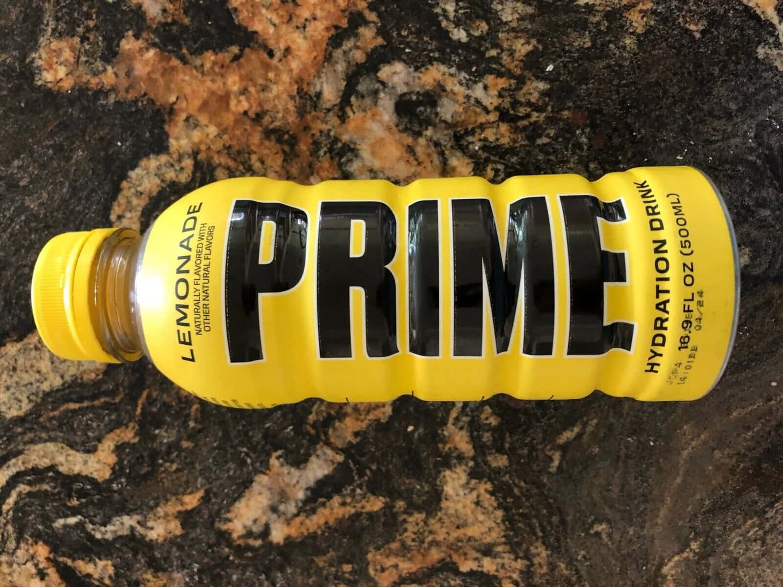  壁紙 — 一個亮黃色的Prime檸檬水補水飲料瓶放在深色斑點花崗岩檯面上。