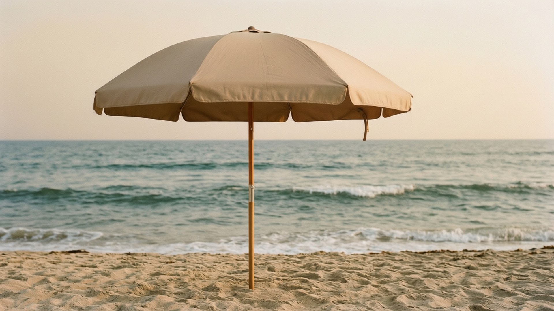 Beach Umbrella on Beige Sand 壁紙 — 一把米色沙灘傘獨自立在沙灘上，柔和的金色光線下，溫柔的海浪拍打著海岸。