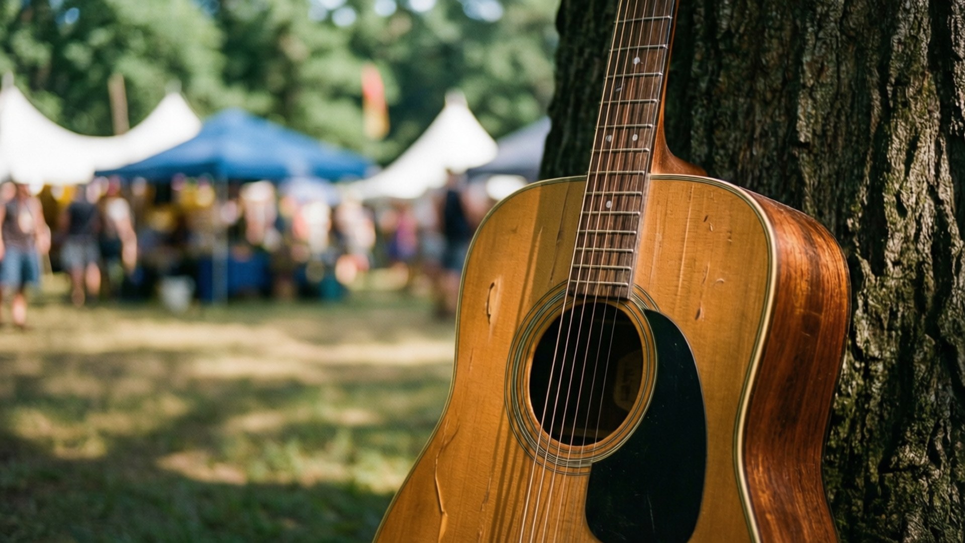 Woodstock Guitar Tree 壁紙 — 一把陽光照耀的木吉他靠在樹幹上，背景有模糊的節日帳篷和人群。