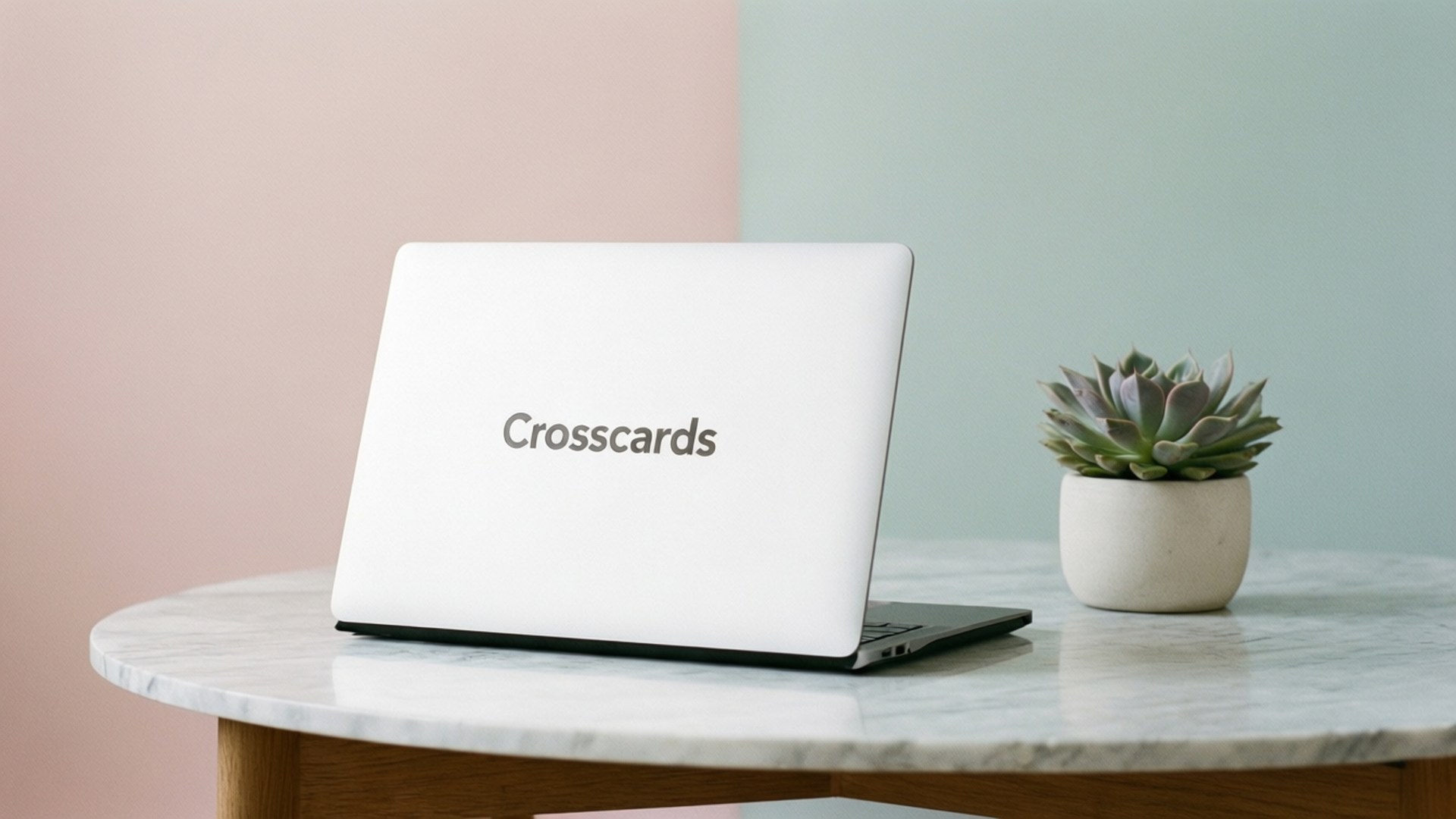 桌布 壁紙 — 一部白色筆記型電腦帶有 'Crosscards' 標誌，放在大理石桌上，旁邊有一盆多肉植物，背景是粉彩粉紅和薄荷綠牆壁。