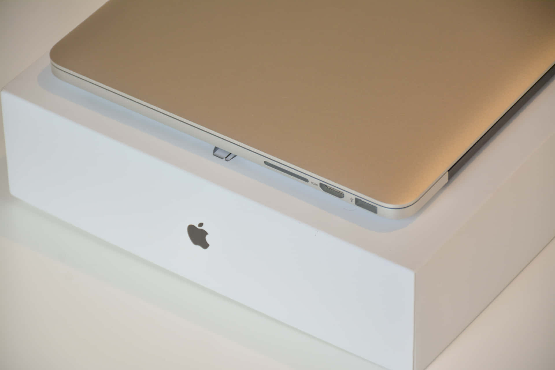 金色 MacBook 放在白色 Apple 盒上，顯示連接埠和標誌 — 美學 MacBook 壁紙 壁紙