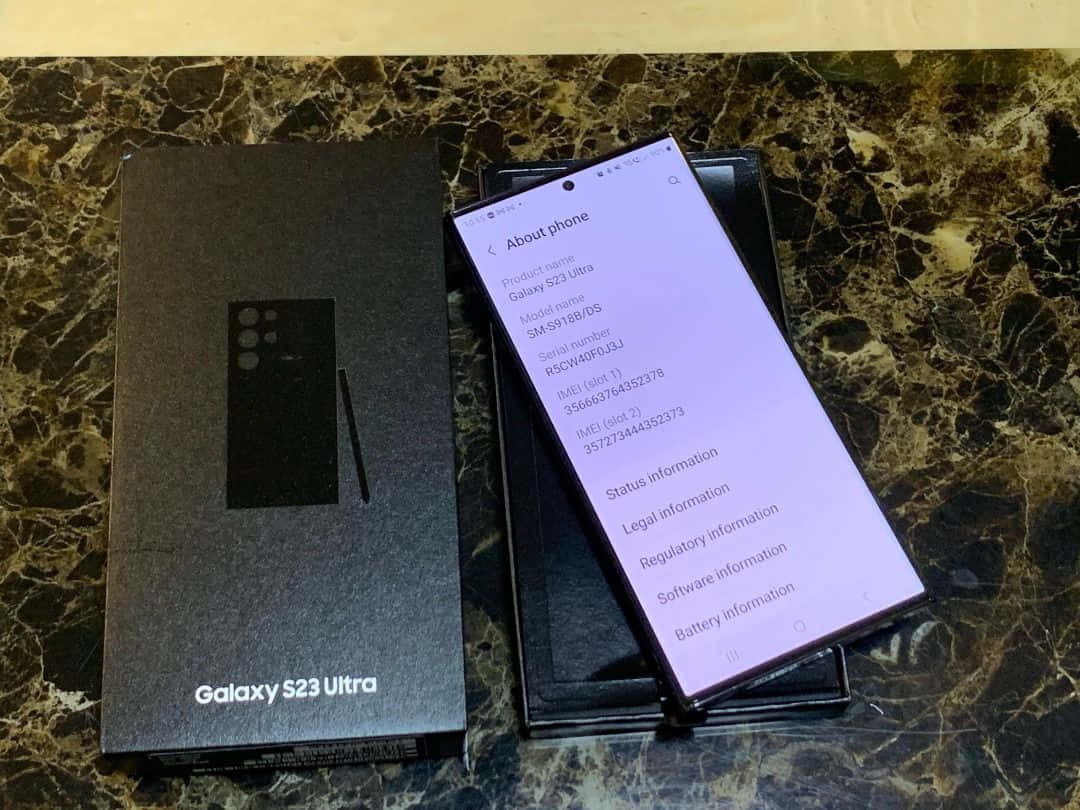  壁紙 — 一部Samsung Galaxy S23 Ultra智慧型手機在深色大理石檯面上，於其黑色盒子旁邊顯示關於手機畫面。