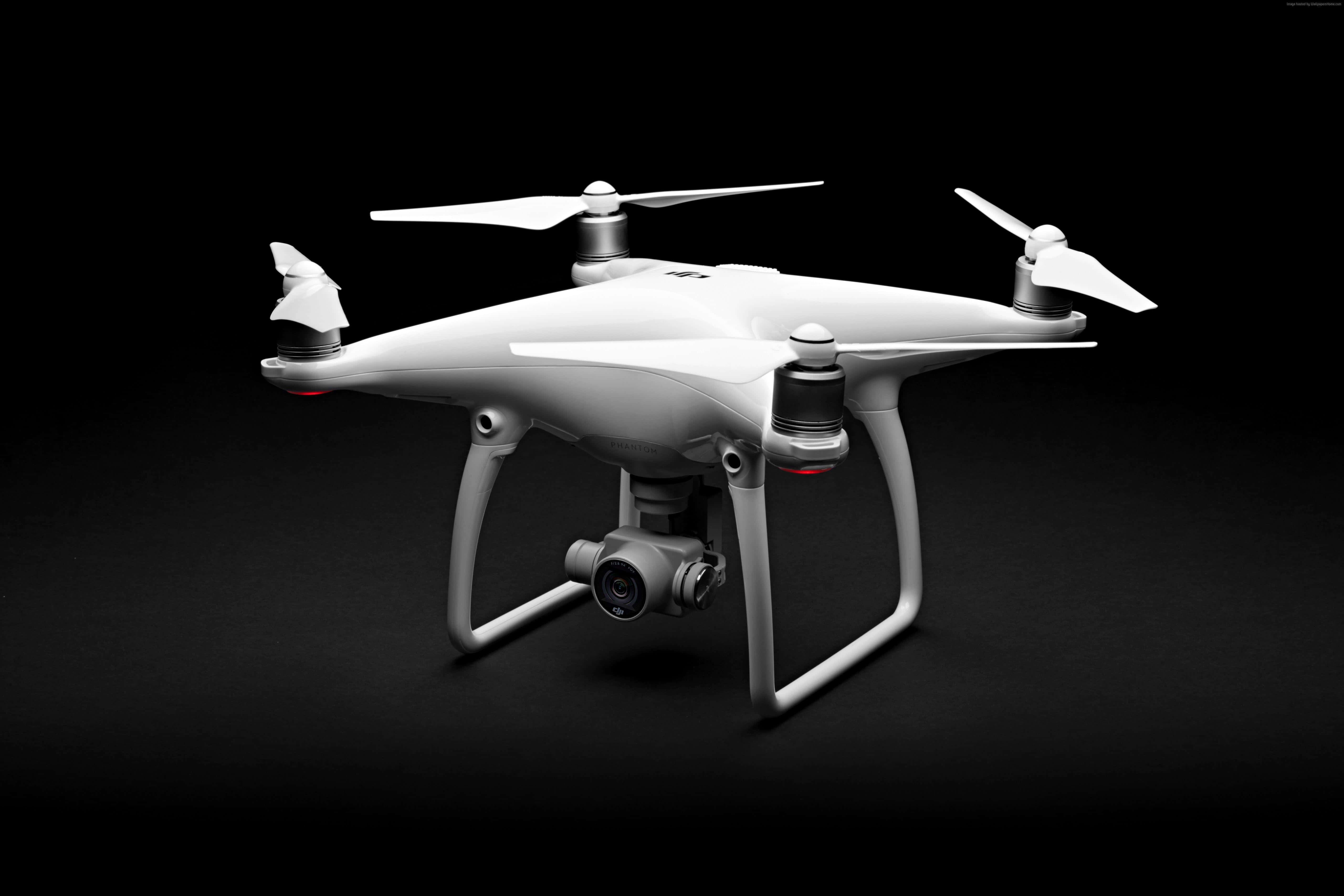 Drone Camera 桌布 壁紙 — 一部時尚的白色無人機，配備四個旋翼和一個安裝好的相機，在純黑色背景前蓄勢待發。
