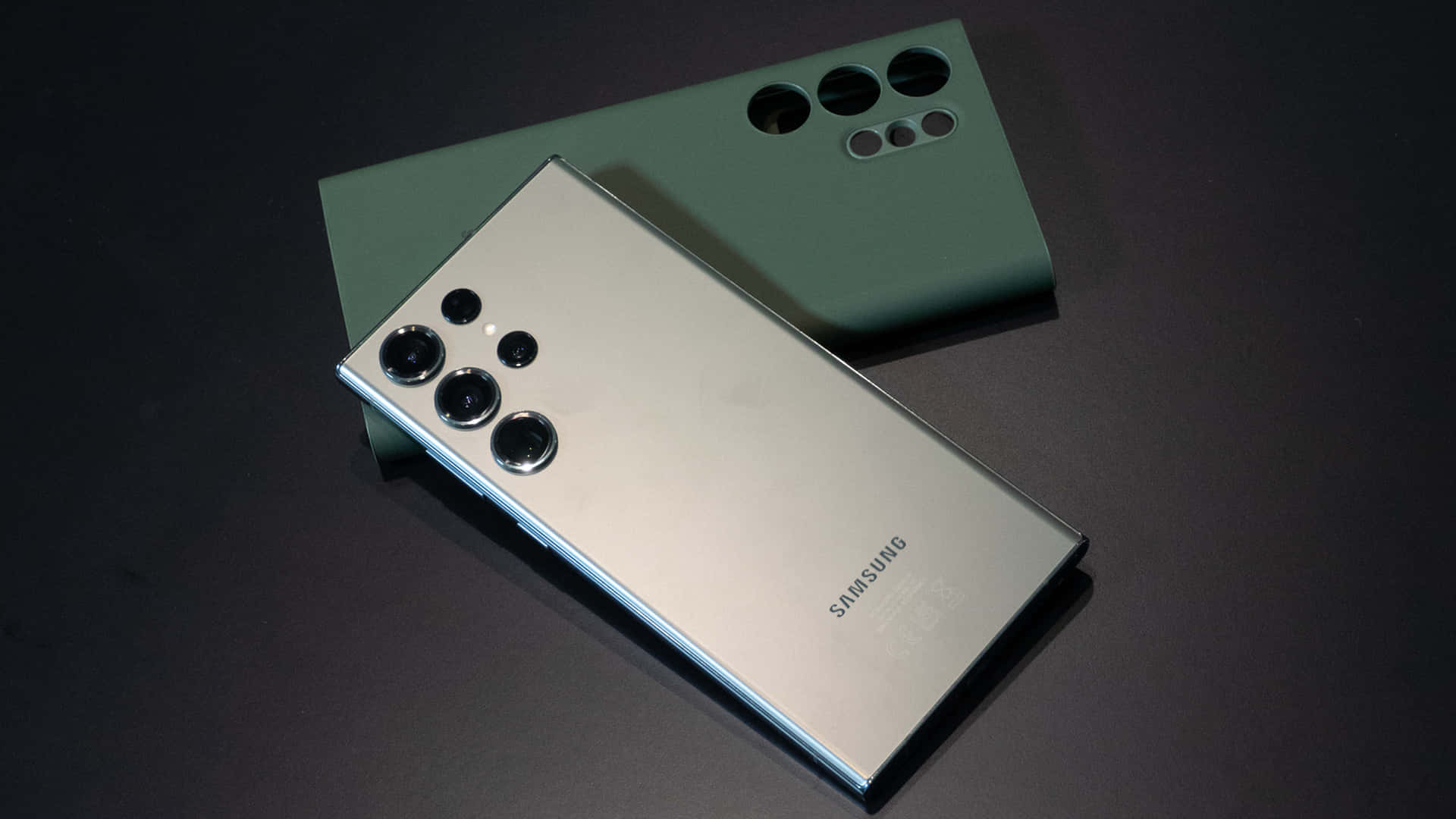 壁紙 — 一部時尚的銀色Samsung智慧型手機斜放在霧面綠色手機殼上，置於深色表面。