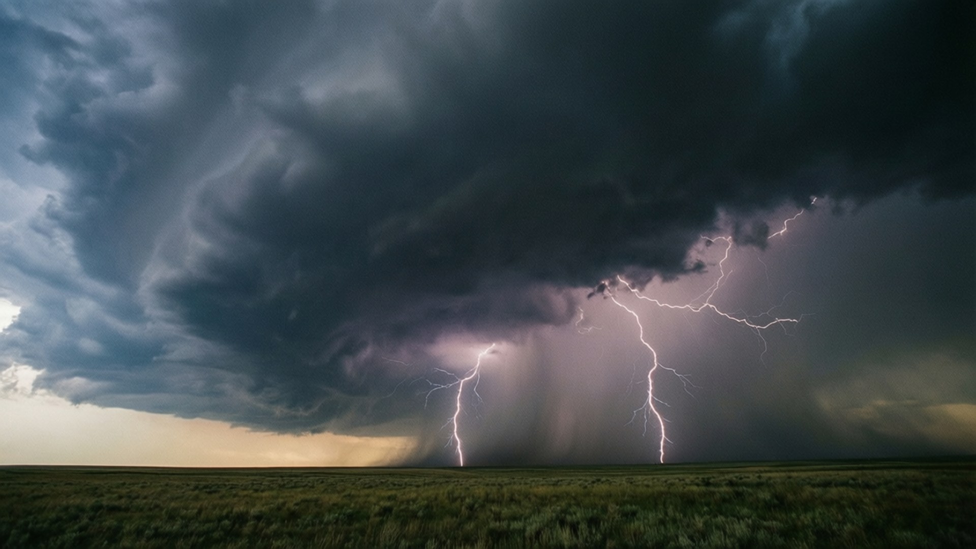 Prairie Thunderstorm 壁紙 — 一道戲劇性的閃電劈開巨大的暴風雲，籠罩著黃昏時分廣闊的草地平原。