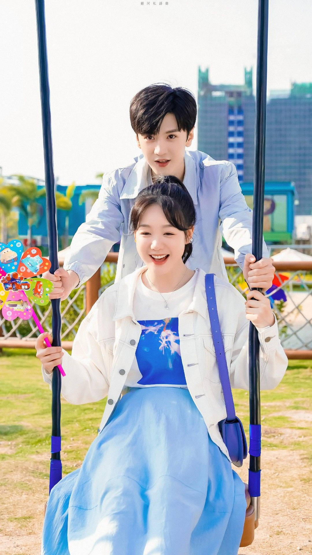 年輕情侶在陽光明媚的城市公園中坐在鞦韆上微笑。 — 韓國 壁紙