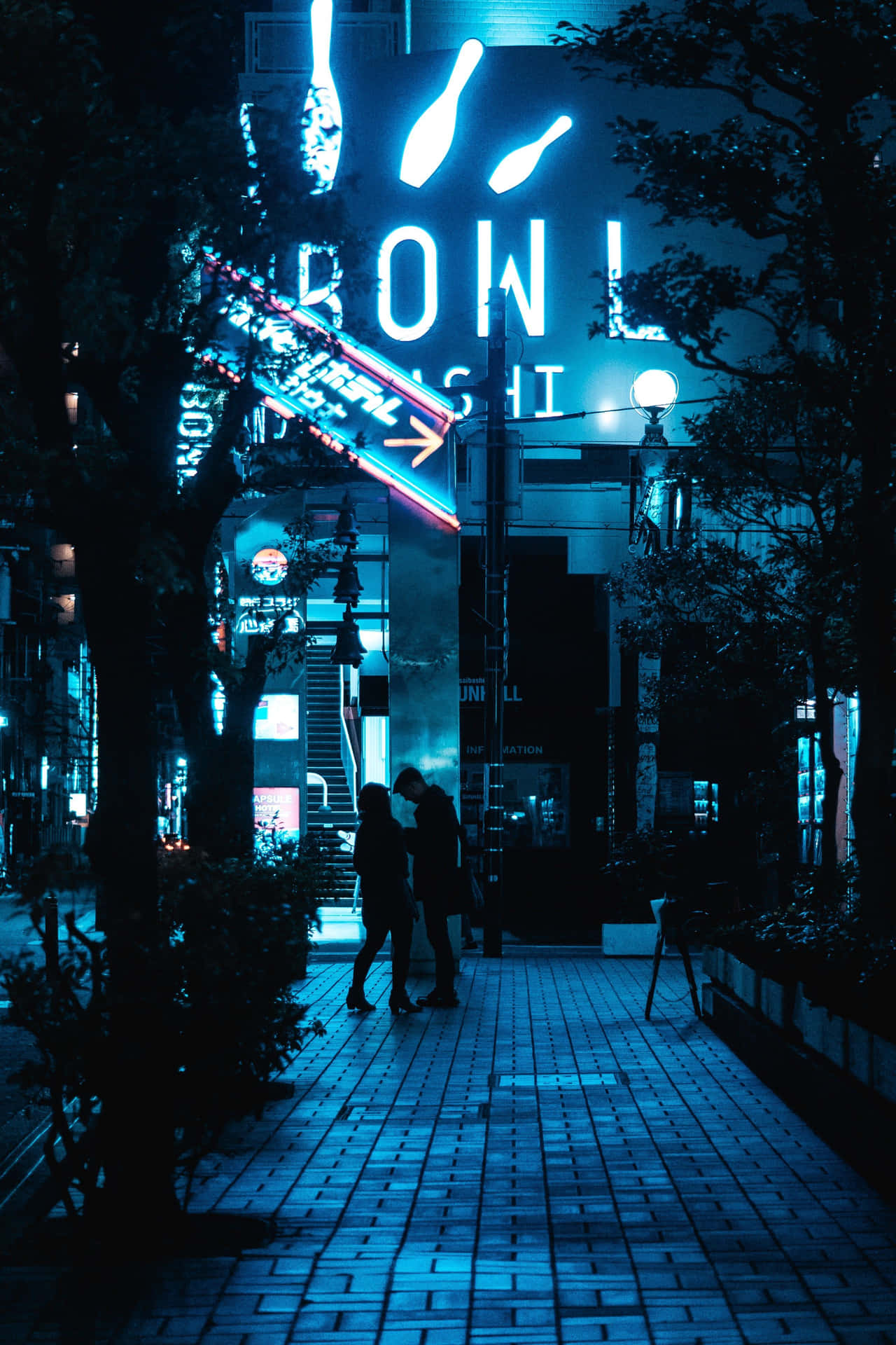  壁紙 — 一對情侶在夜晚寧靜的藍色燈光城市人行道上，在發光的霓虹燈招牌下行走。