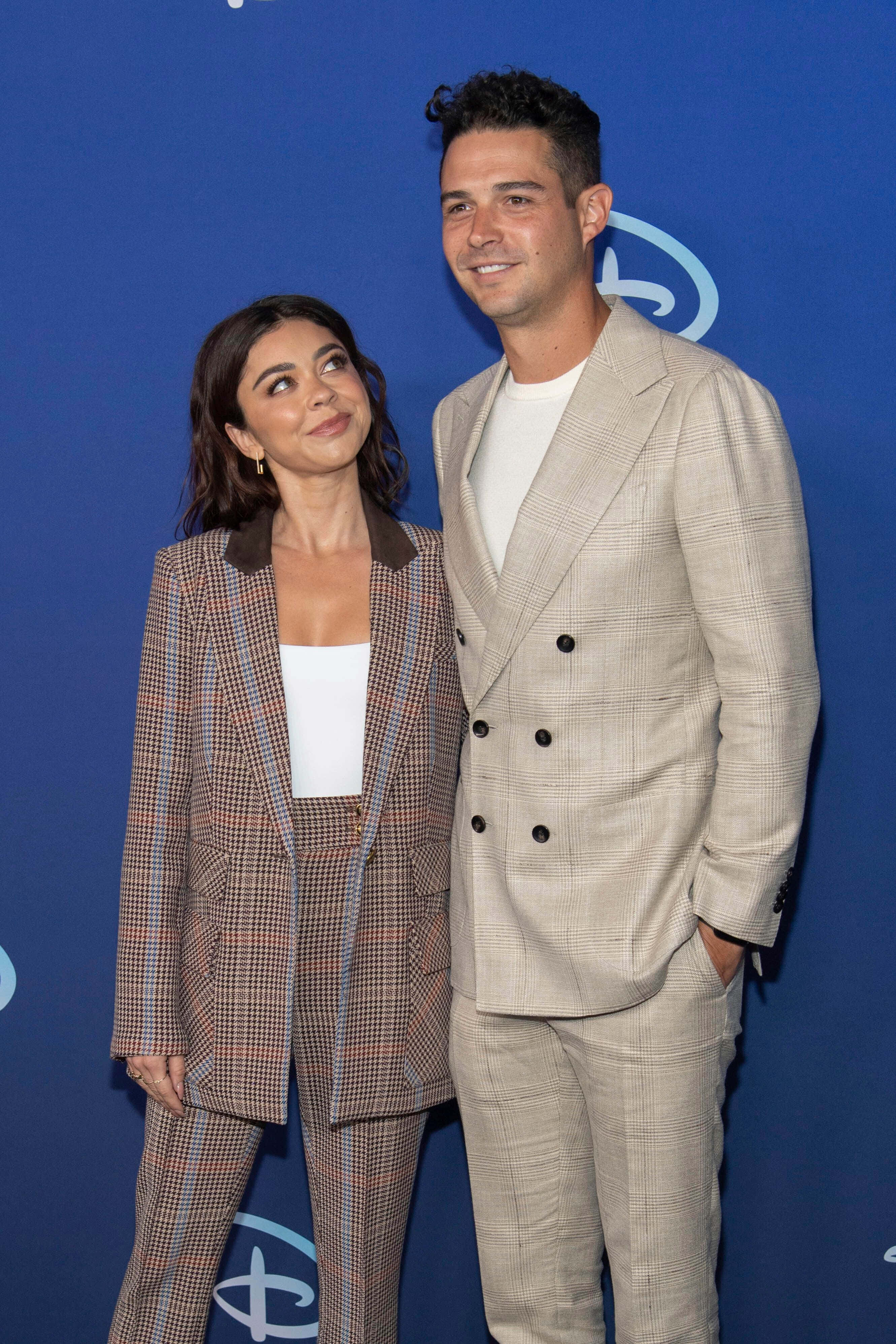 Sarah Hyland 桌布 壁紙 — 一對時尚情侶在藍色迪士尼背景前合照，兩人都對著鏡頭溫暖微笑。