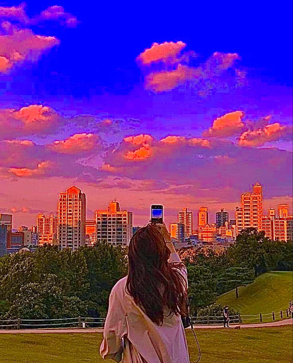  壁紙 — 一個長髮的人正在拍攝沐浴在充滿活力的紫色和橙色日落色調中的城市天際線。
