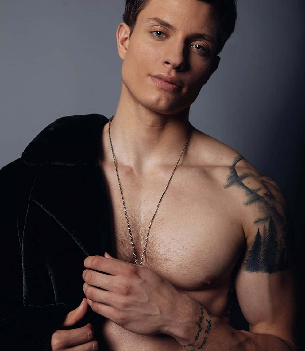 Matt Rife 桌布 壁紙 — 一個赤裸上身、有刺青、穿著天鵝絨外套的男人，在深灰色工作室背景前自信地擺姿勢。