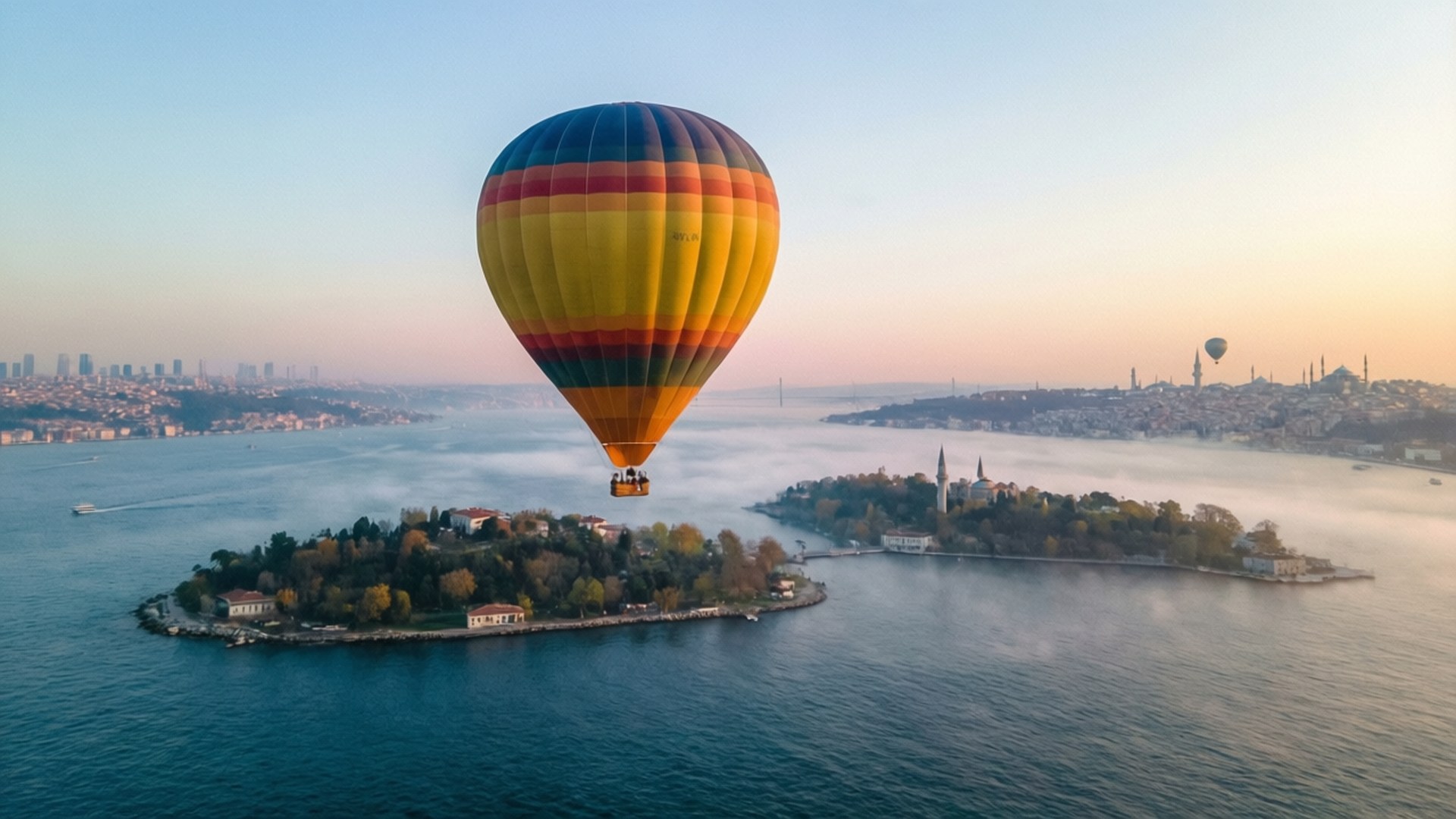 Balloons Over Princes' Islands 壁紙 — 一個充滿活力的多色熱氣球漂浮在黎明時分靠近樹木覆蓋的島嶼和遠處城市天際線的霧氣水域上空。